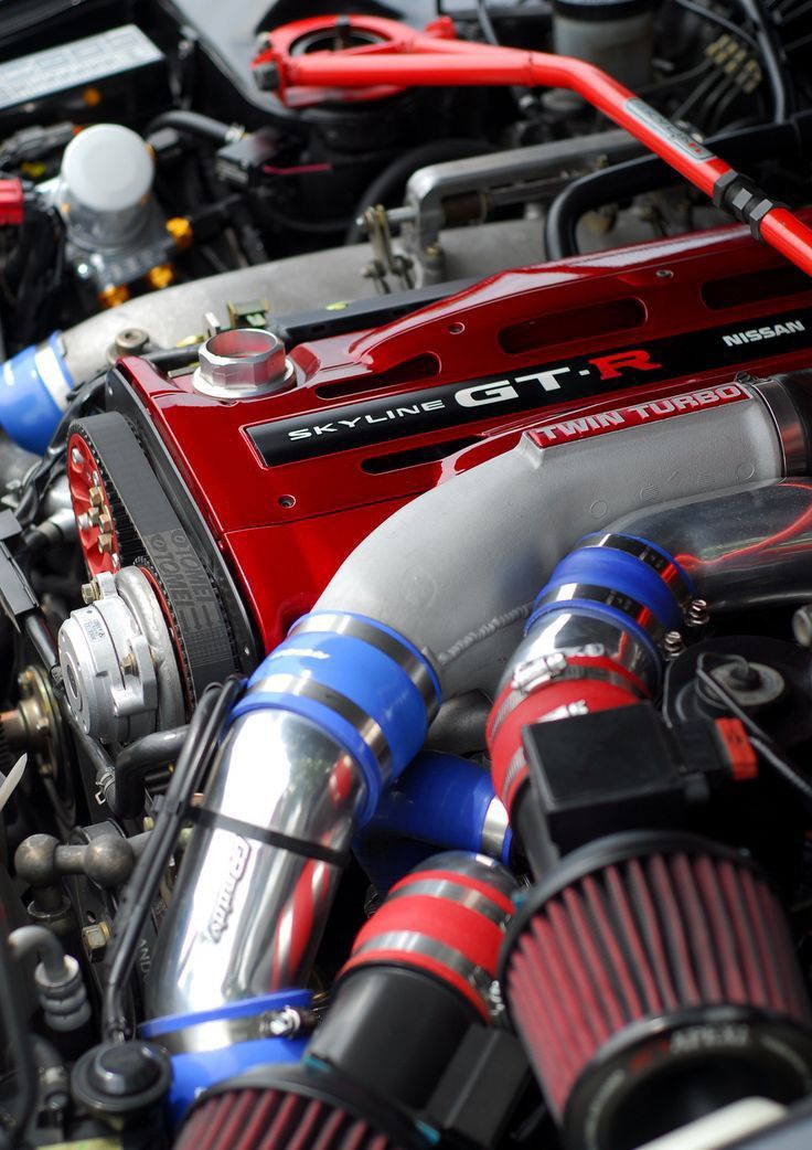 Close-up of a Nissan Skyline GT-R engine with red cover, twin turbo setup, and blue intake pipes.