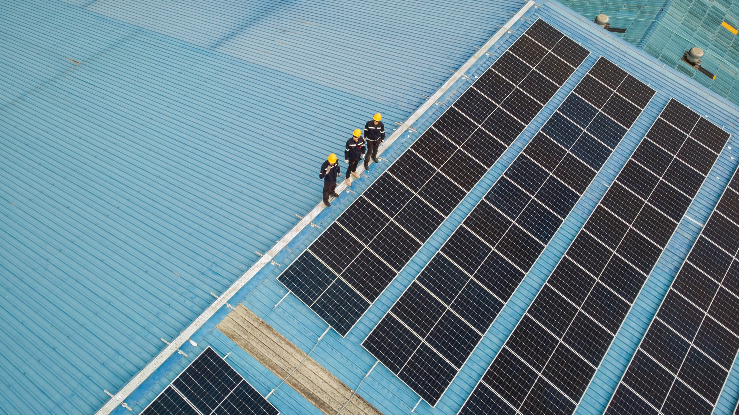 Aerial view of engineer worker walking on rooftop checking on solar cell panels installed on roof of the factory with professional team. Electric power industry renewable energy.