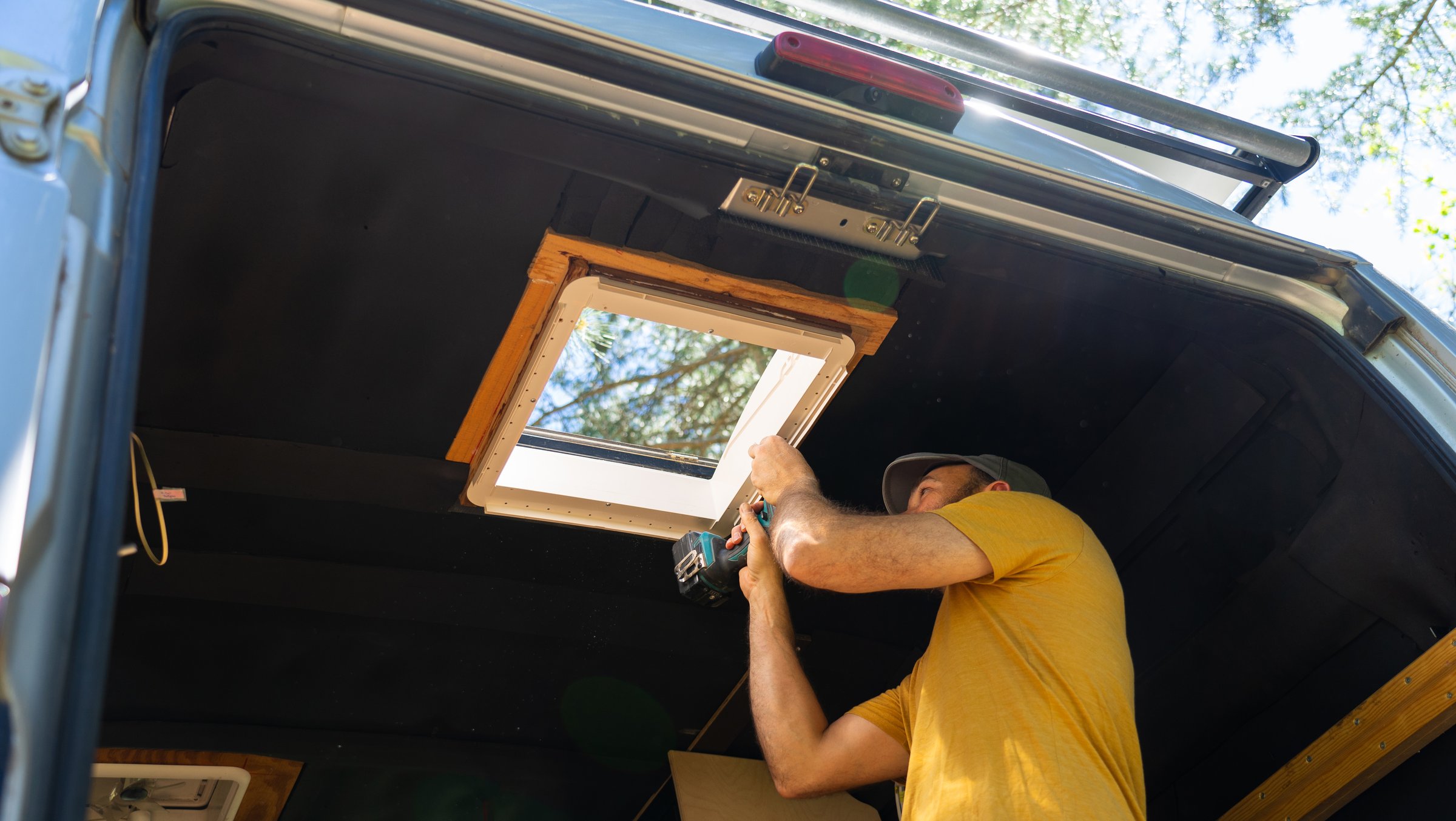 Handyman installing a camper van roof vent using a cordless drill during a sunny day