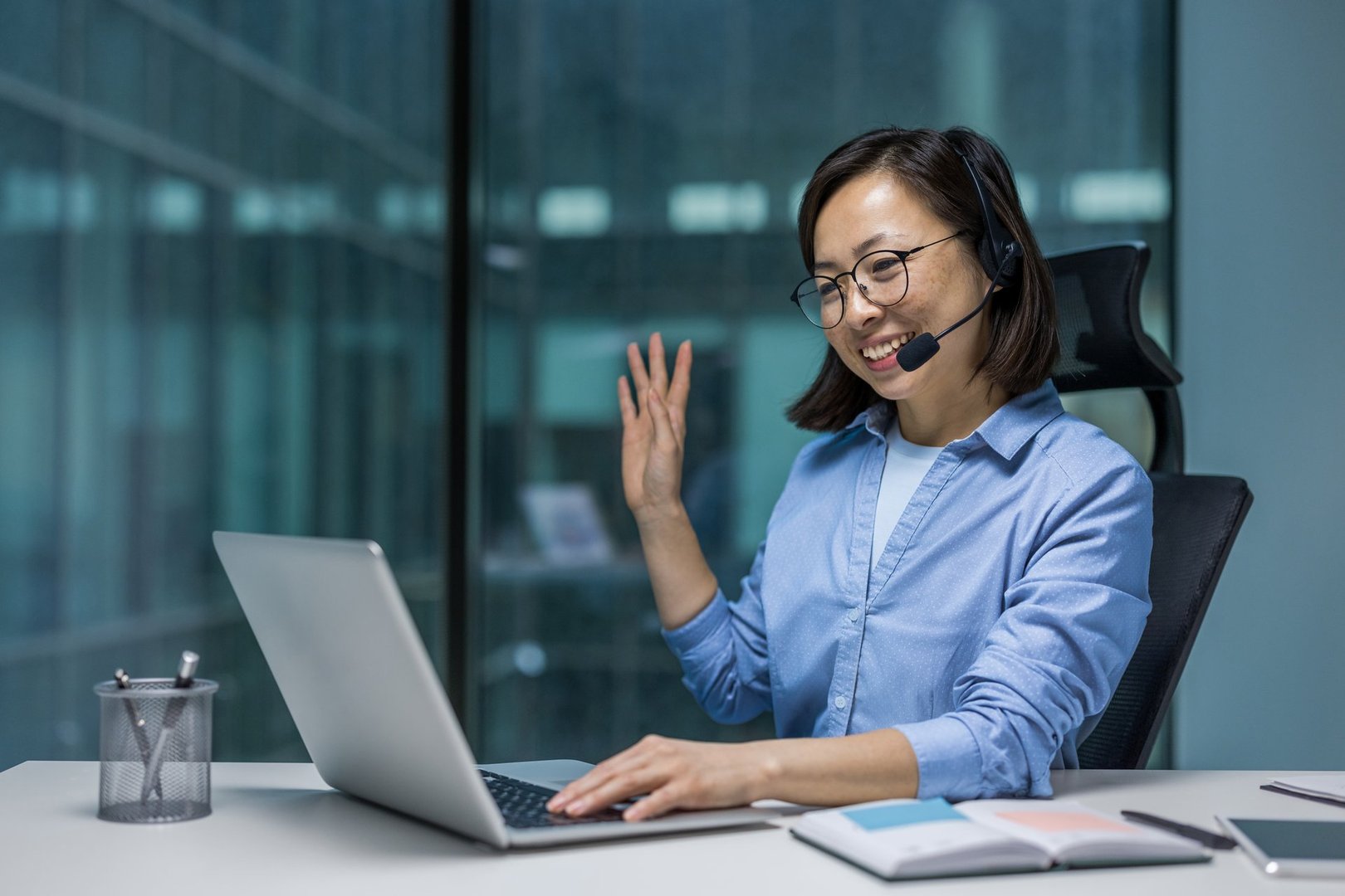 Woman with headset talking using laptop for video call, Asian woman smiling happily consulting customers remotely, support worker at work place inside office.