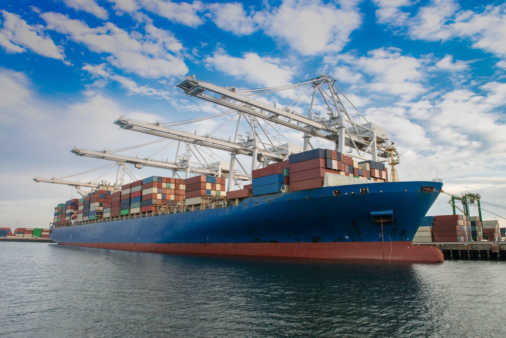 A large container ship is being unloaded in a commercial dock during the late afternoon.