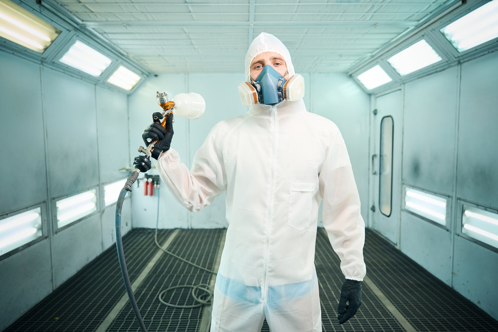 Mechanic wearing protective suit standing with a gun in chamber. Car service station concept