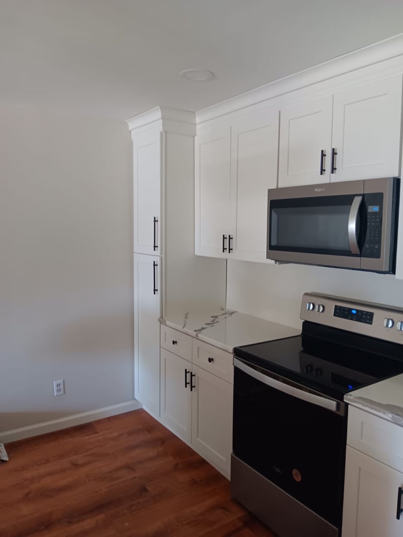 Modern kitchen with white cabinets, stainless steel microwave, and oven on hardwood floor.