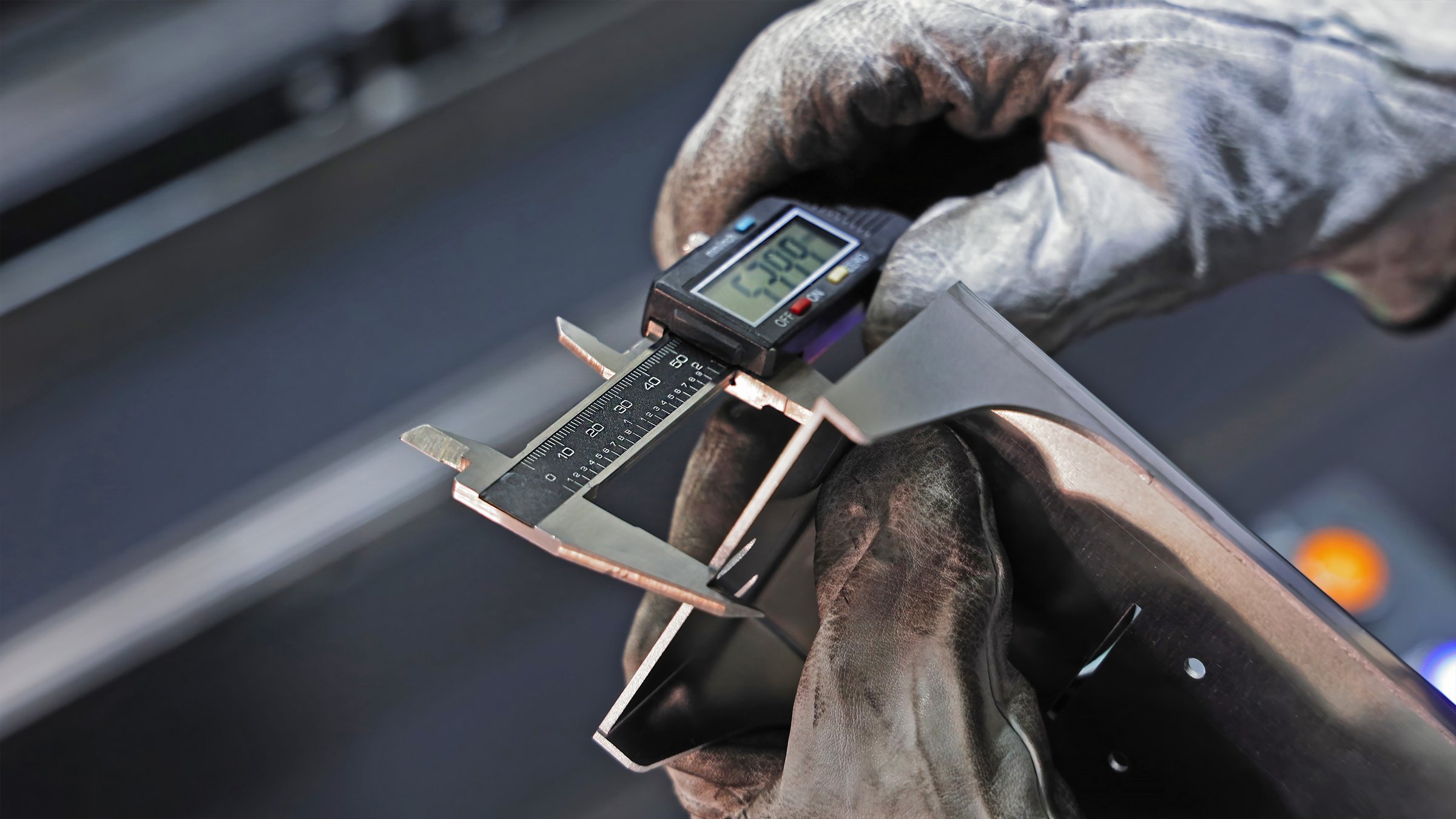 Worker measuring metal part with digital caliper. A gloved hand is using a digital caliper to precisely measure the width of a metallic component, with the LCD screen showing a reading of 53.09 millimeters