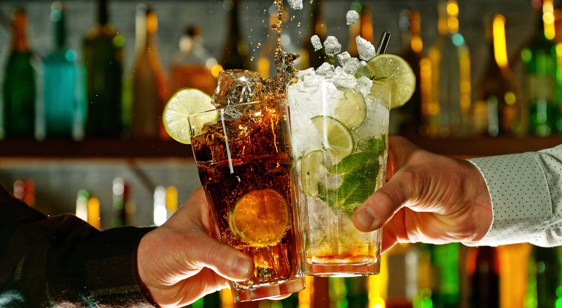 Close-up view of a two glasses of cocktails in hands. Cocktail glasses clinking at bar or pub.