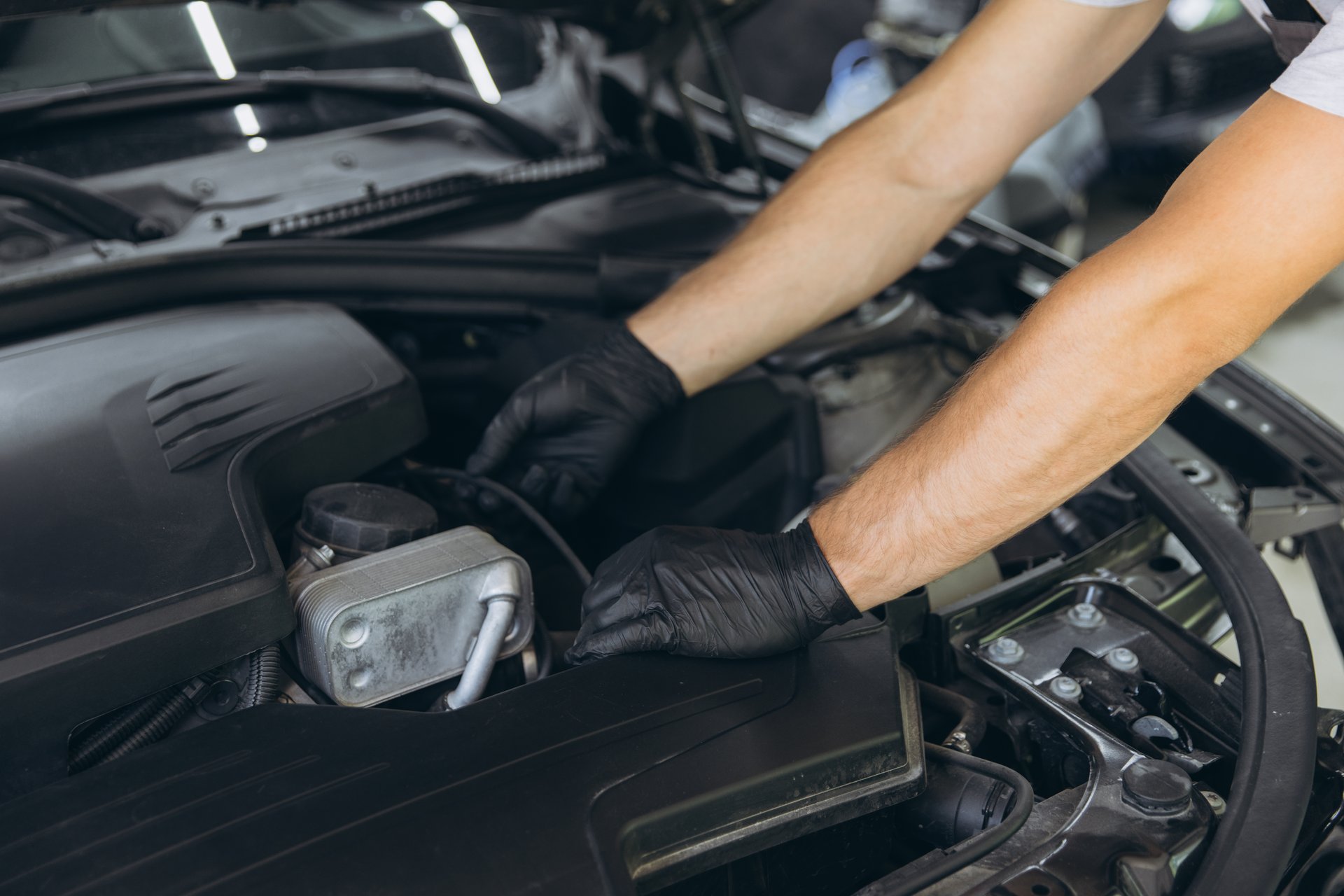 Mecánico reparando motor de coche con guantes de nitrilo resistentes a grasas.