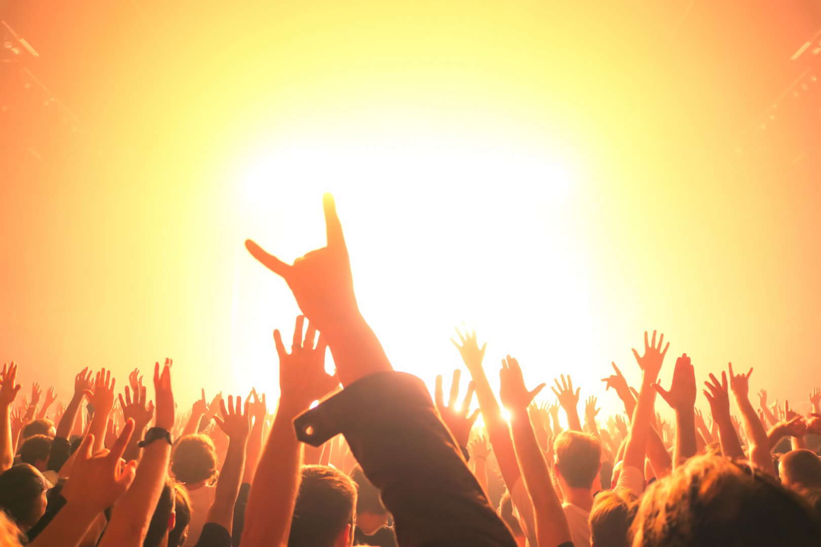 Crowd with raised hands at concert bathed in bright golden stage lights