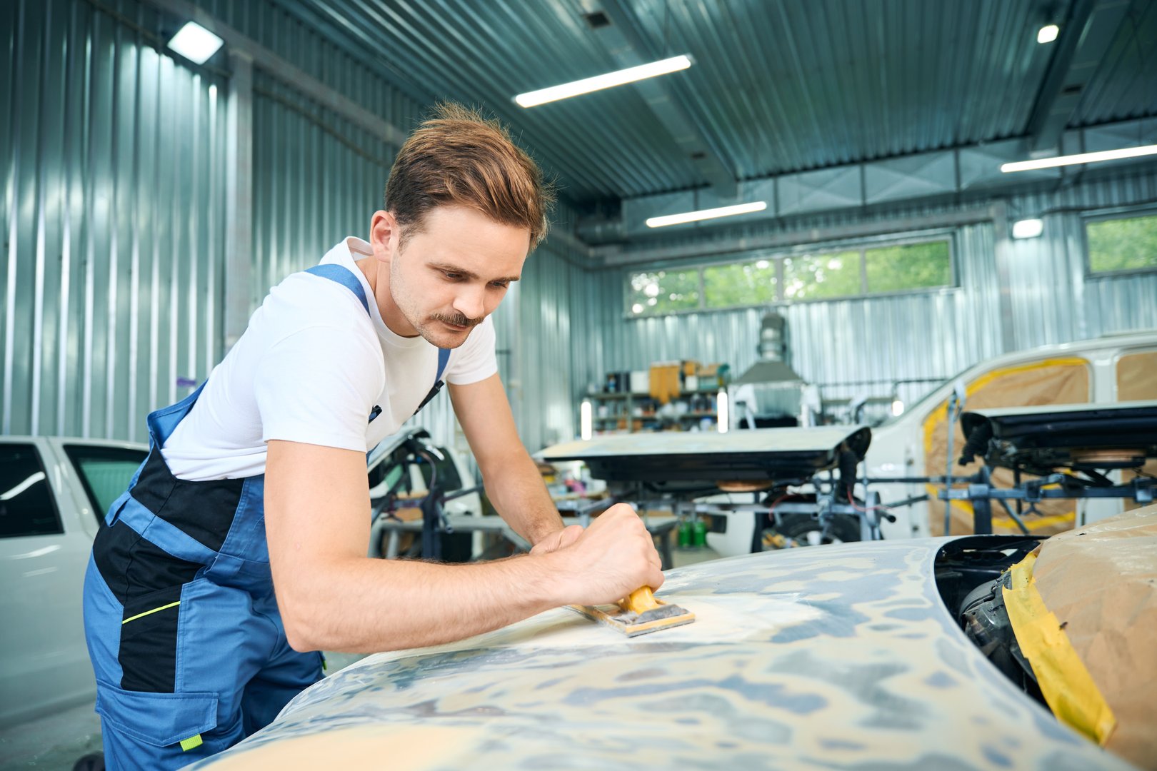 Male worker working with a grinding tool in workshop. Repair of car concept