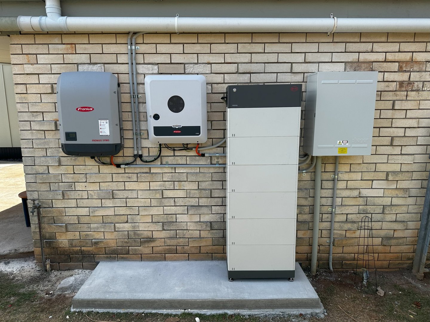 Solar power system components mounted on a brick wall, including inverters and a battery storage unit.