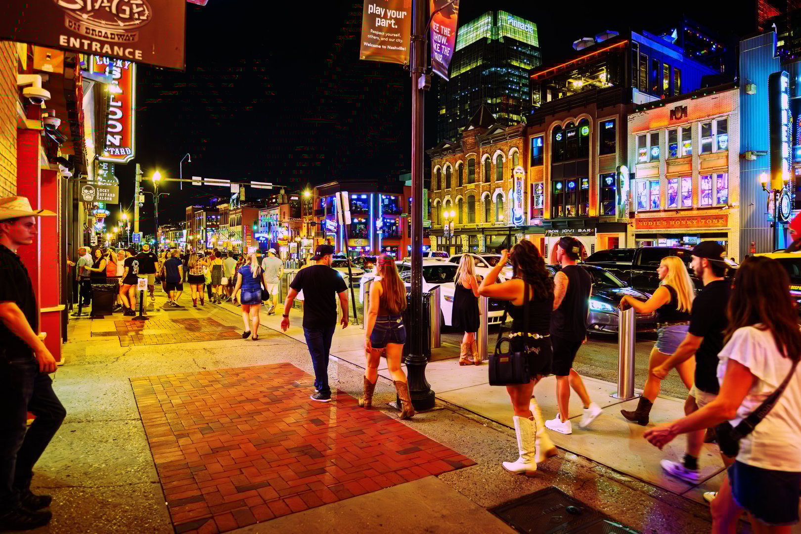 Late night visitors enjoy the lively atmosphere, bars, clubs and cafes, under the neon lights of Broadway Street in downtown Nashville, Tennessee. Broadway, especially Lower Broadway, is the heart of Nashville's entertainment and music scene. It's a bustling street known for its honky-tonks, live music venues, and vibrant atmosphere. This area, between the Bridgestone Arena and the Cumberland River, is a major tourist destination and a place where music lovers gather.