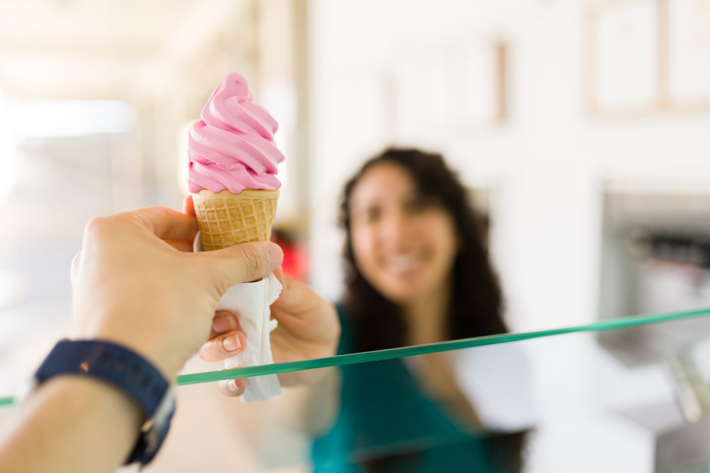 Woman worker selling a delicious cold strawberry ice cream cone to a happy female customer behind the counter at the gelato shop