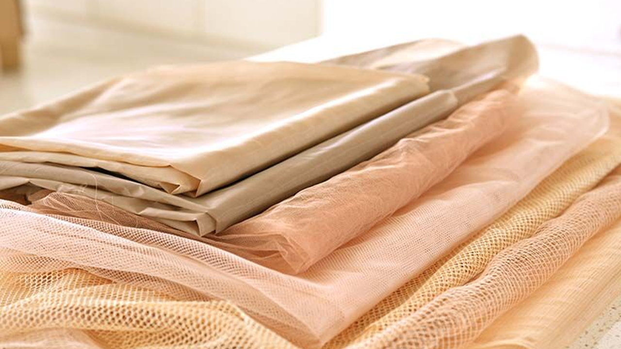 A stack of folded beige and peach-colored sheer and net fabric on a table.