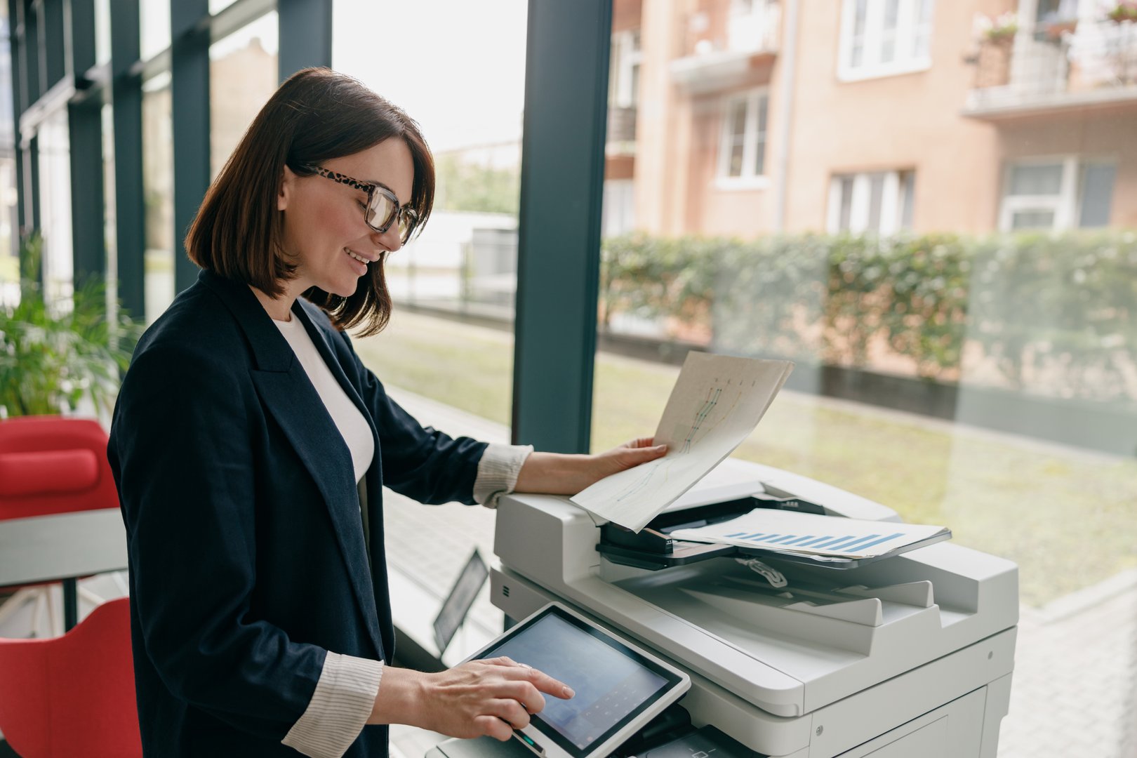 A professional businesswoman is utilizing a photocopier to reproduce documents in a contemporary office environment