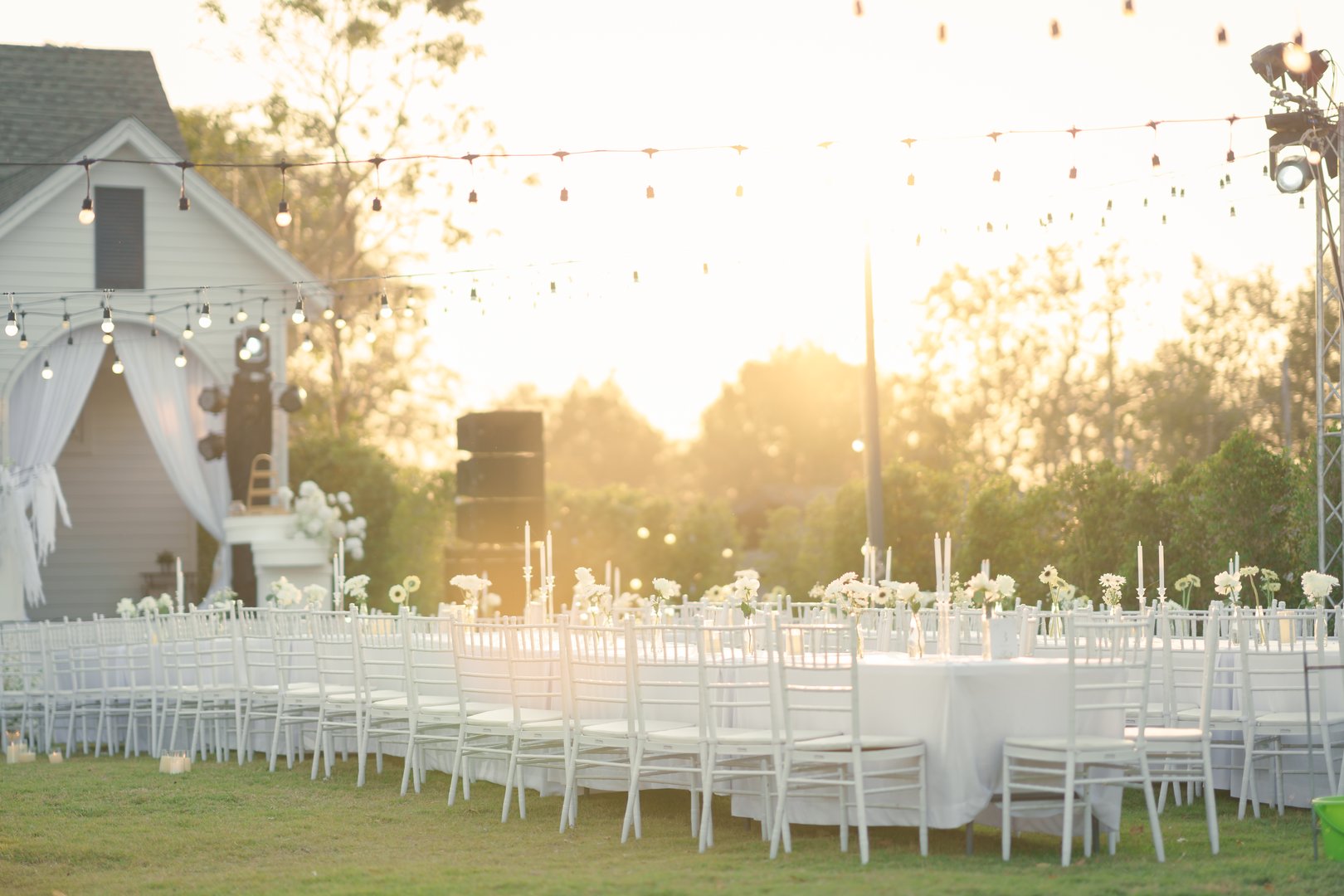 Elegant outdoor wedding long table with candle, white rose flower and white chairs in the garden on marriage festive