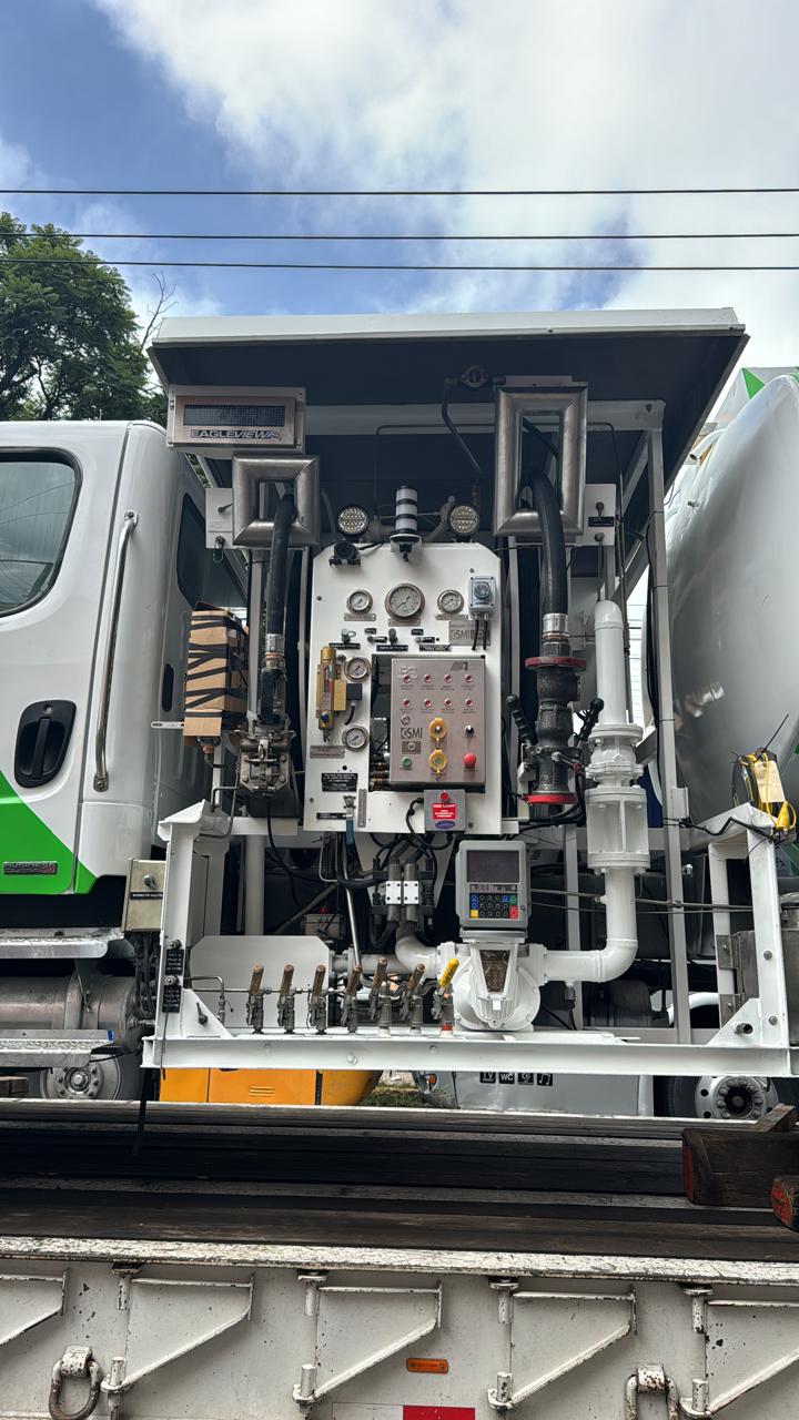 Industrial machinery on a trucks flatbed featuring complex controls, gauges, pipes, and connected cabling.