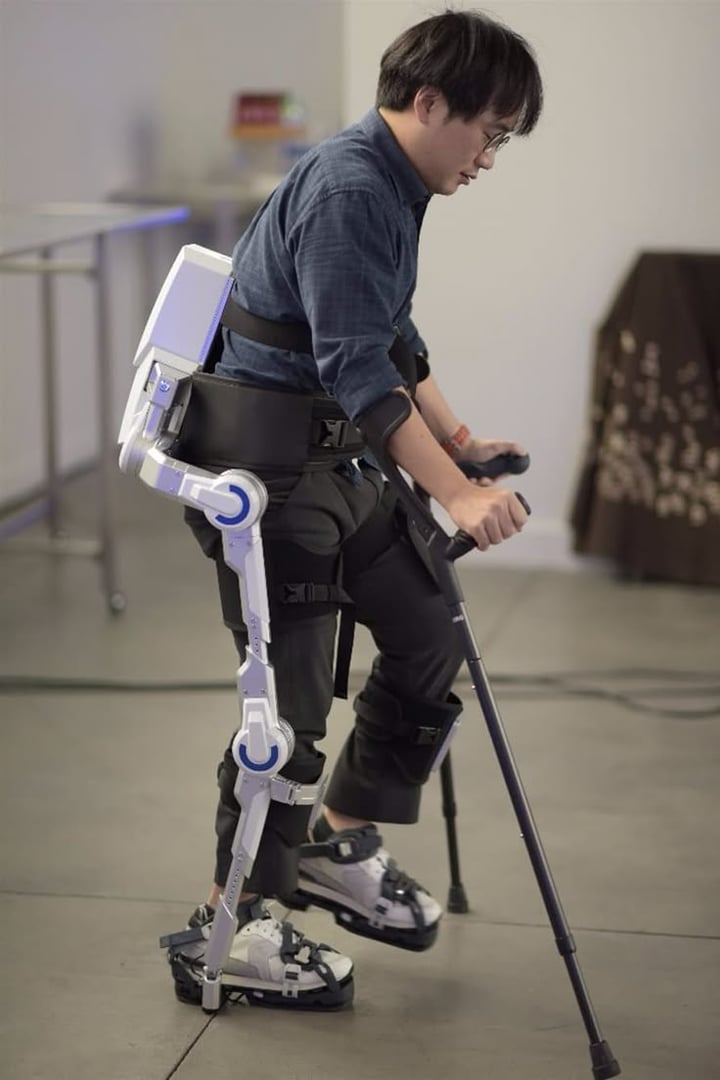 A person using a futuristic exoskeleton suit with crutches, demonstrating wearable assistive technology indoors.