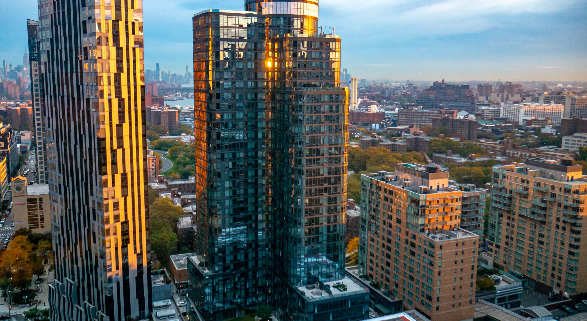 Morning in NYC at sunrise, high angle view with orange light reflecting on modern skyscraper buildings. Brooklyn, New York, with the Manhattan skyline in the distance.
