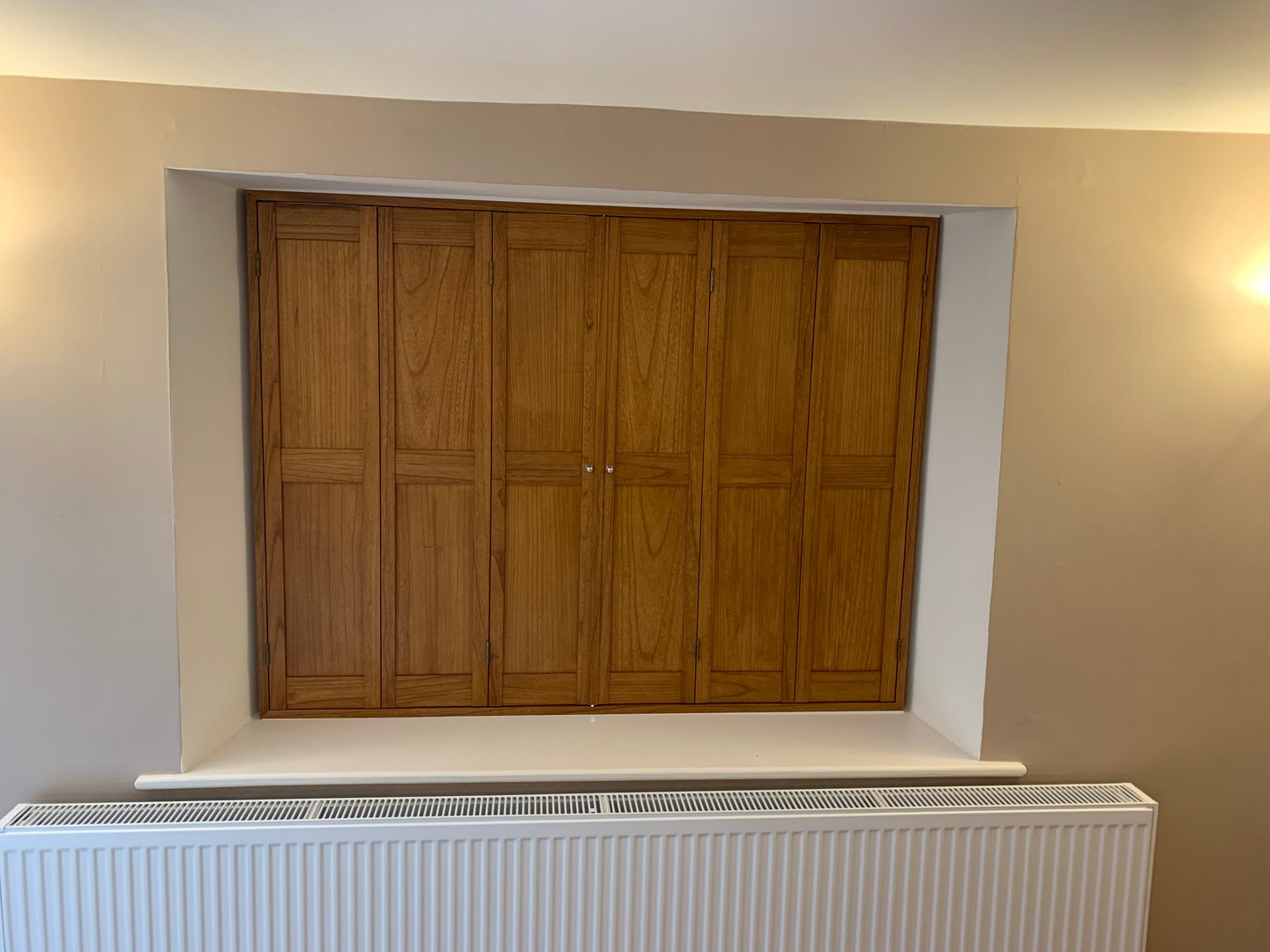 Wooden cabinets above a white radiator in a beige-walled room.