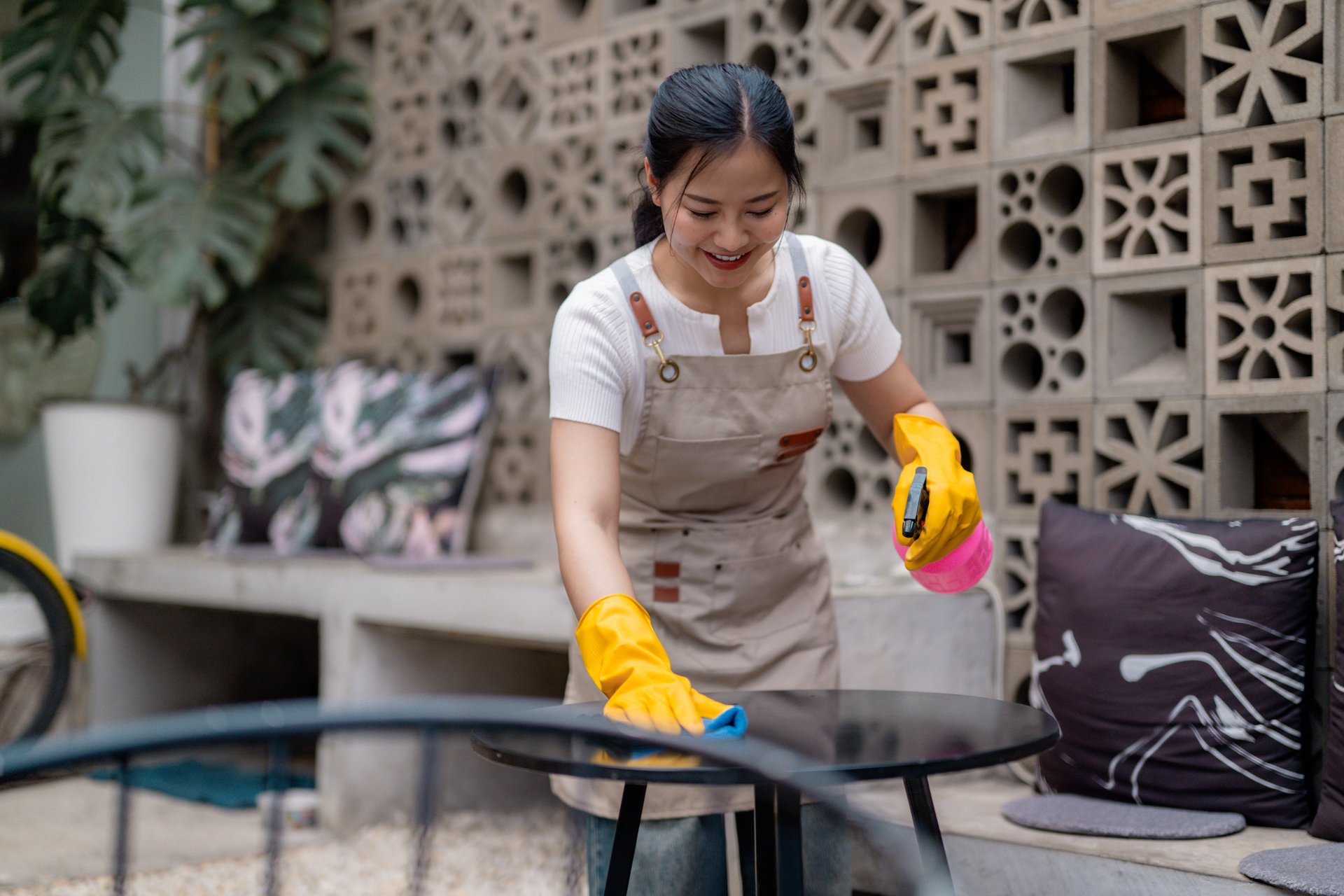 Cafe worker sanitizing outdoor table surface using disinfecting spray, wiping thoroughly during shift