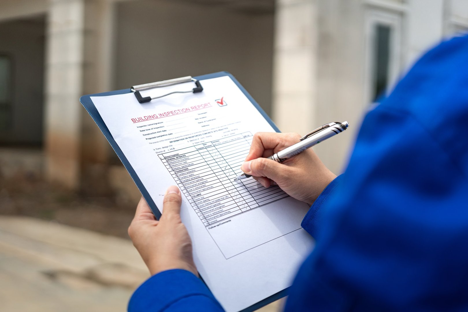 A construction foreman is checking on building quality checklist report during inspecting at the house construction site (as background). Industrial working scene, close-up with selective focus.