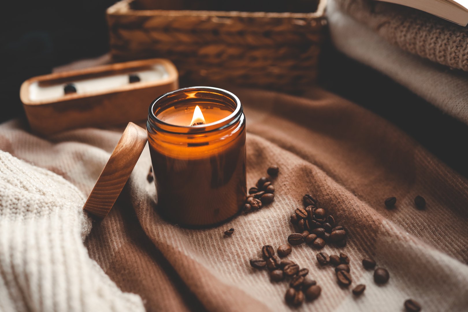 A burning candle with the smell of coffee, an open book and a stack of cozy sweaters, an aesthetic picture.