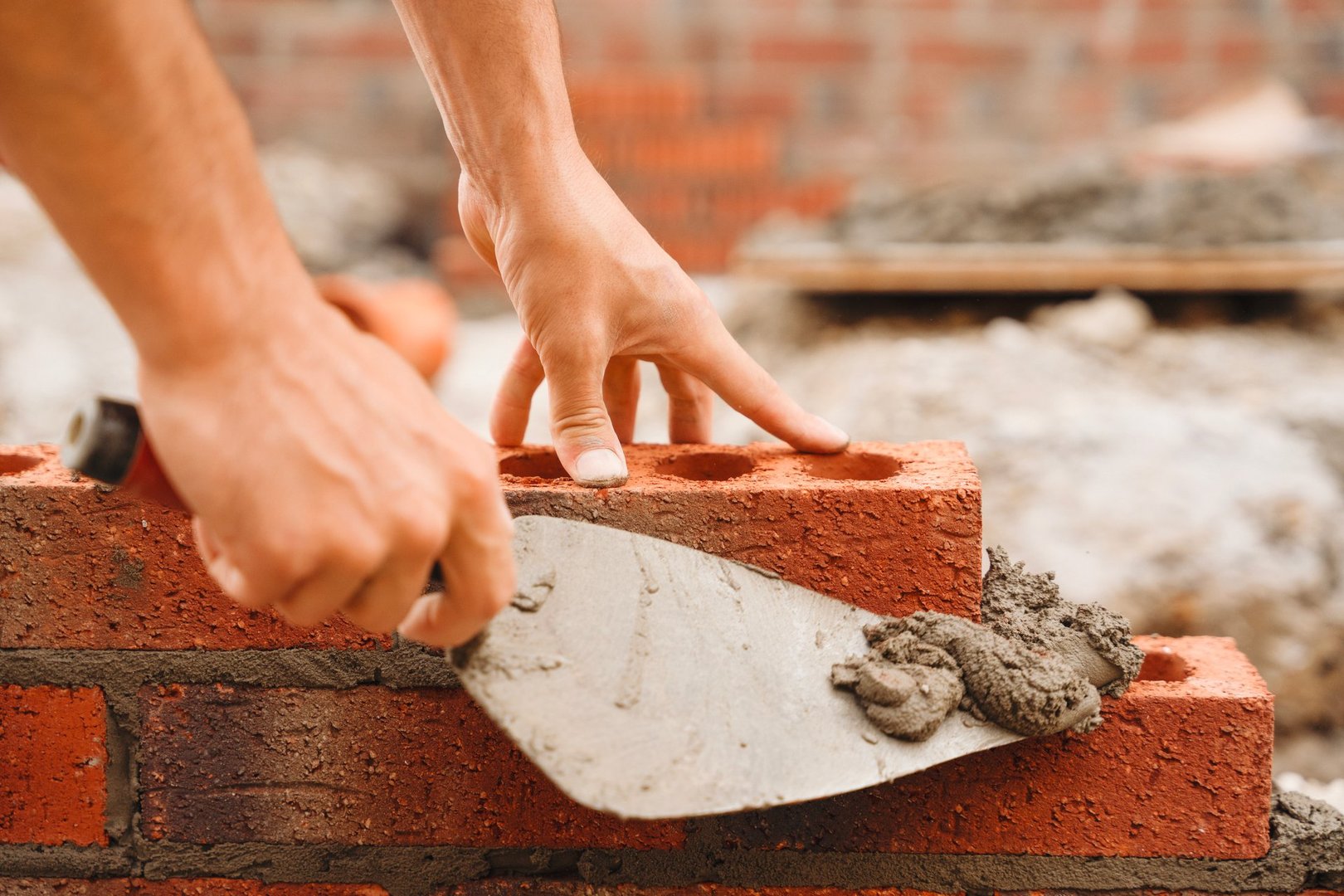 A construction worker expertly places bricks in a wall, using a trowel to apply mortar, demonstrating skilled craftsmanship at a construction site in bright daylight.