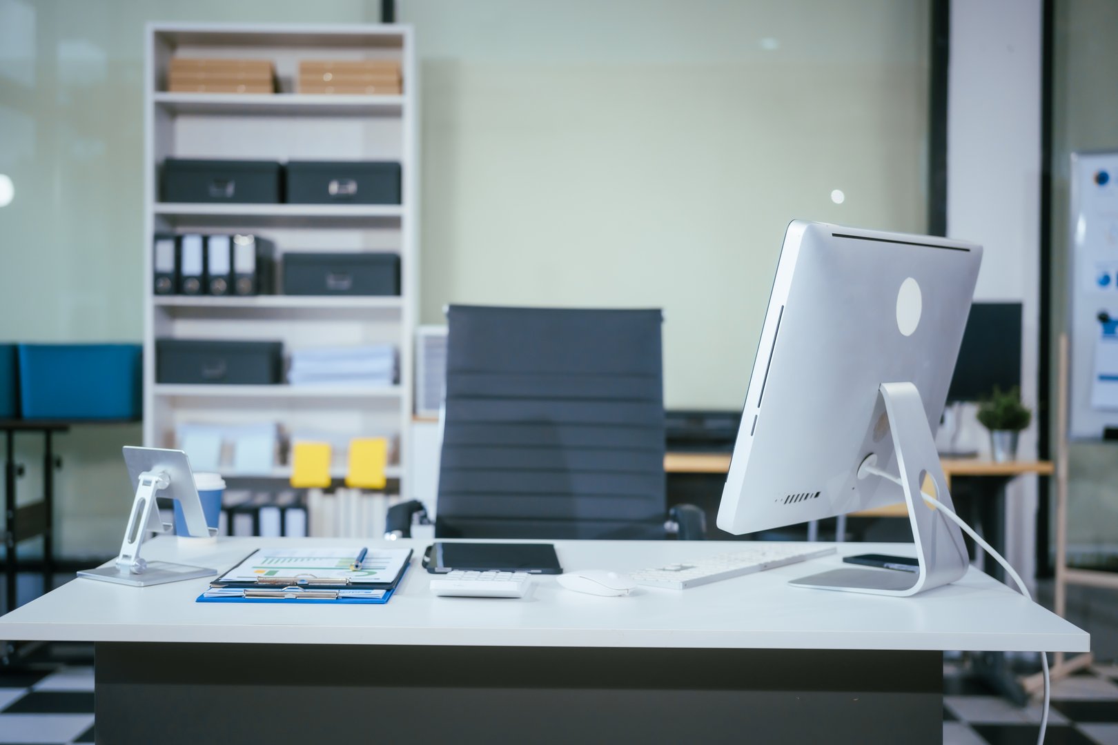 An empty desk with a computer displaying a graph on the screen, a tablet placed on the table, and a chair positioned near. The workspace is neat and ready for use