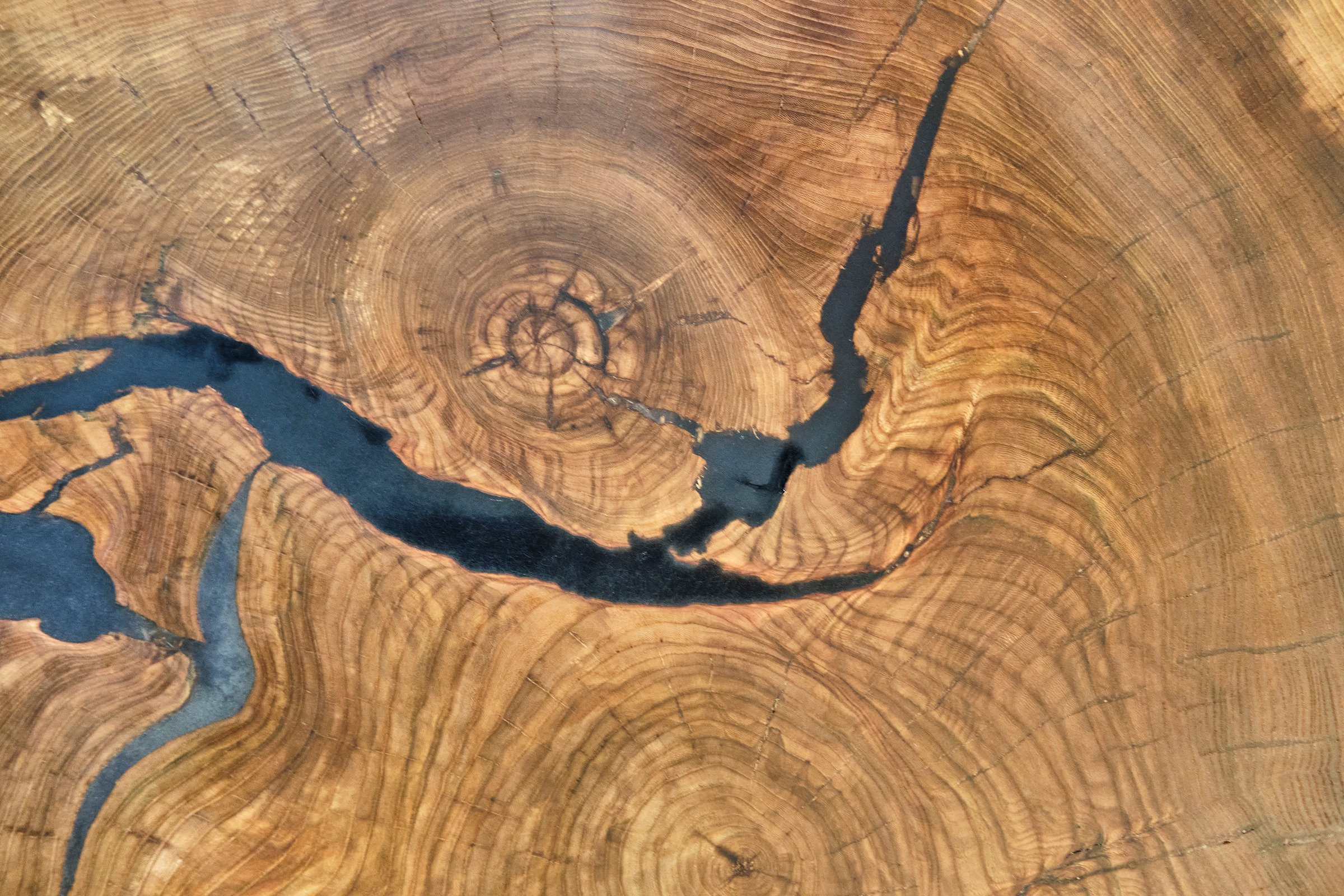 Close-up of wooden tabletop featuring natural cracks filled with epoxy resin. Intricate wood grain and organic patterns create unique abstract background.