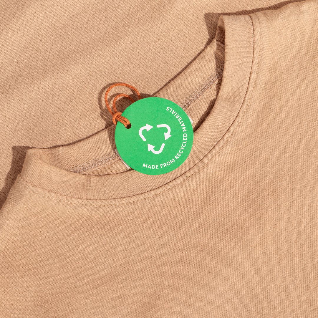 Beige tshirt and Green paper label with inscription "Made from recycled materials". Ecology concept. Mockup.