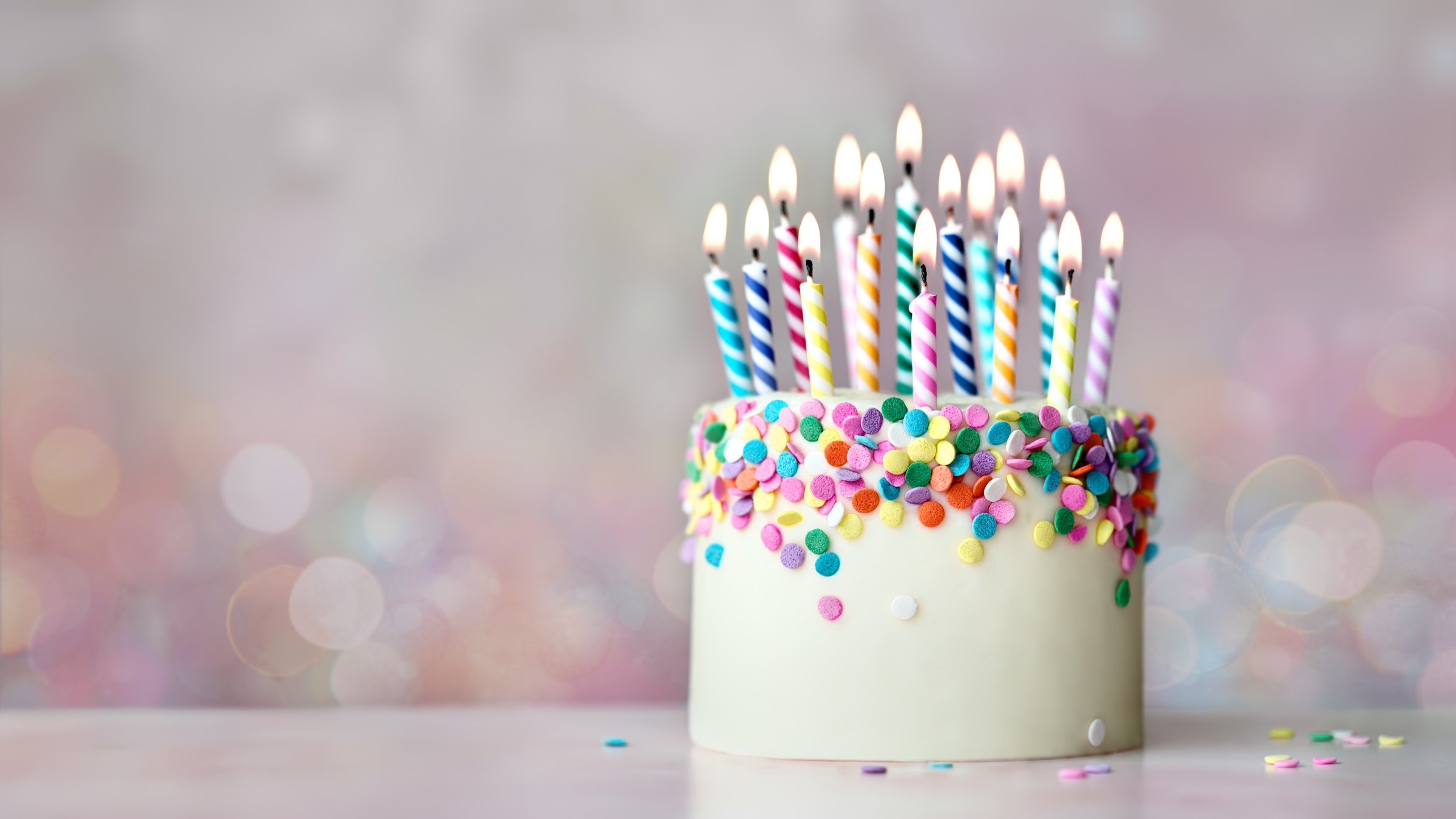 Colorful celebration birthday cake with sugar sprinkles and colorful birthday candles against a background of defocused fairy lights