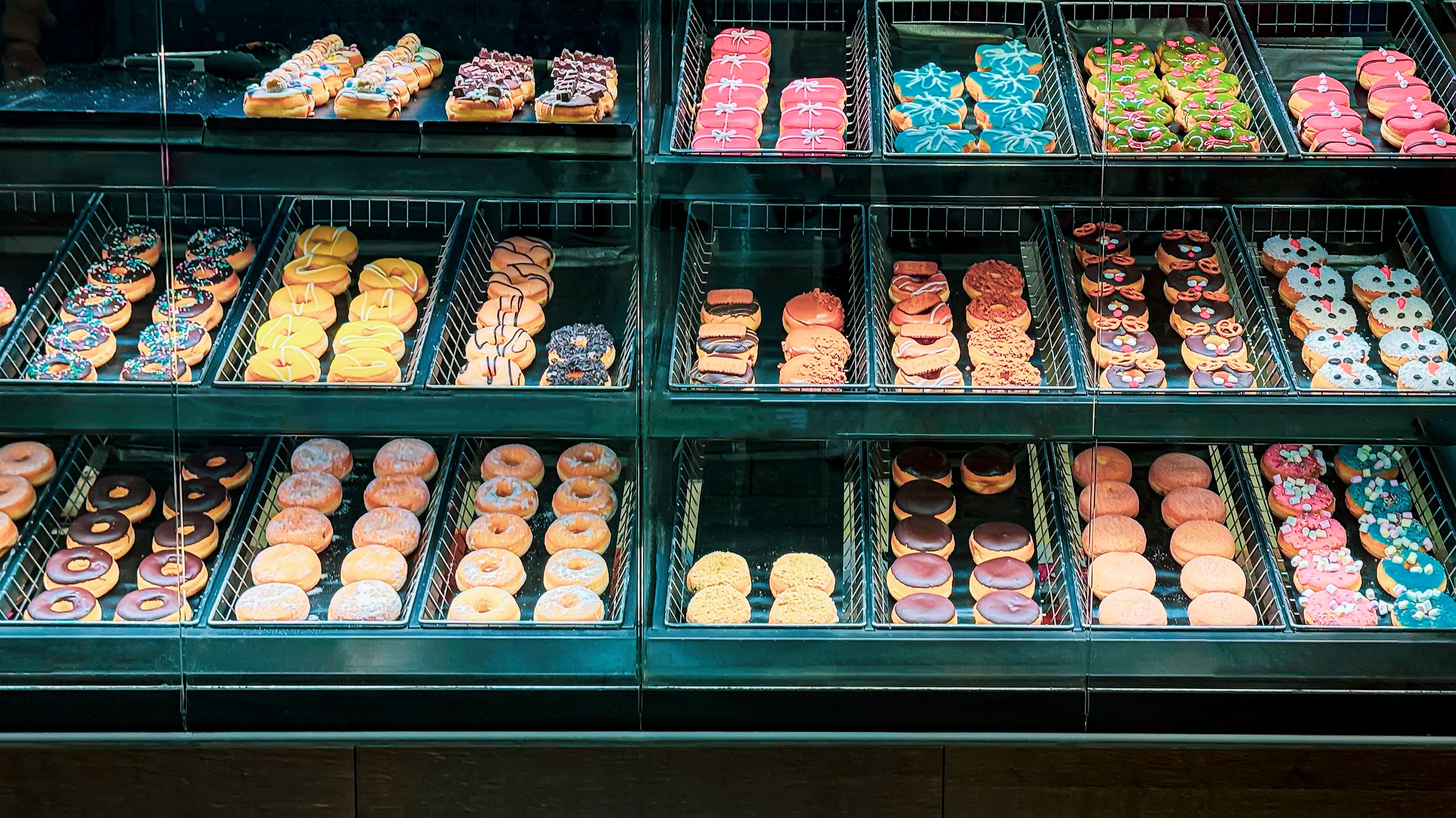 Display case filled with colorful donuts of various shapes and decorations. A variety of sweet bakery treats