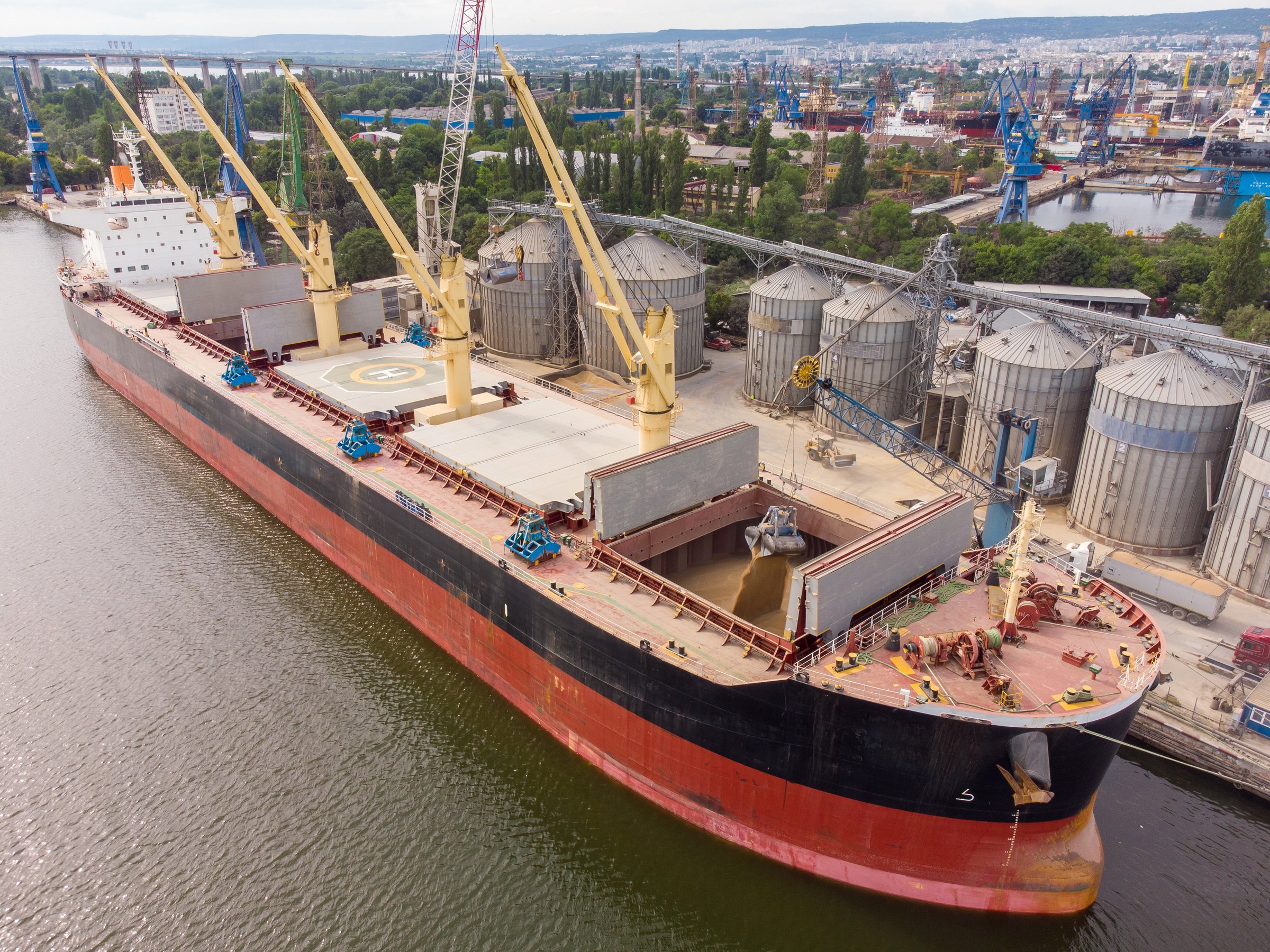 Loading grain into holds of sea cargo vessel in seaport from silos of grain storage. Bunkering of dry cargo ship with grain. Aerial top view