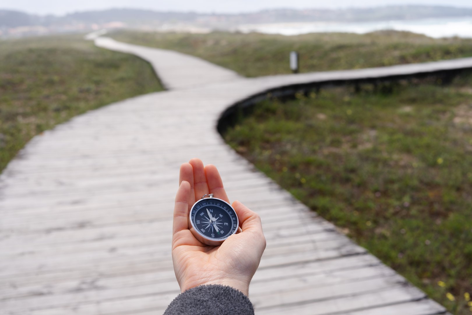 A person holding a compass on a wooden boardwalk. The promenade has two paths.