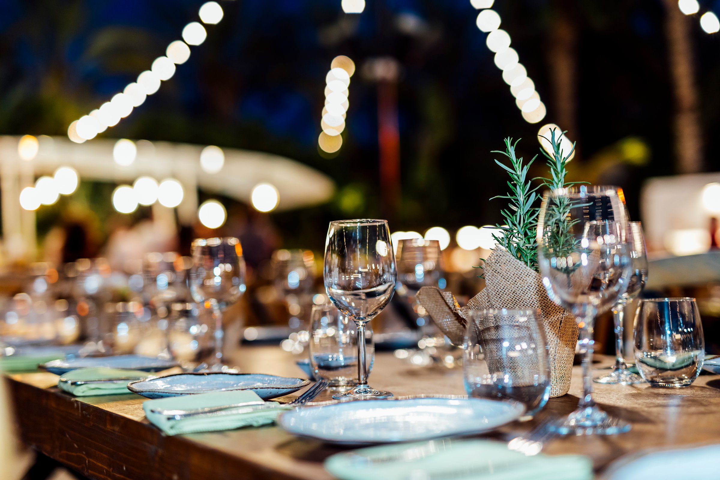 Romantically set dinner table with wine glasses and floral centerpiece, perfect for a wedding, elegant party, or outdoor evening celebration. Warm lights and soft bokeh create an intimate and luxurious atmosphere.