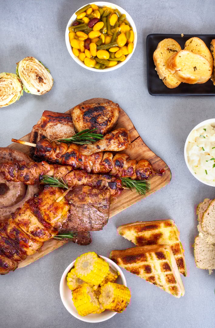 flat lay of Traditional South African Braai meal on table, meat and sides on grey surface