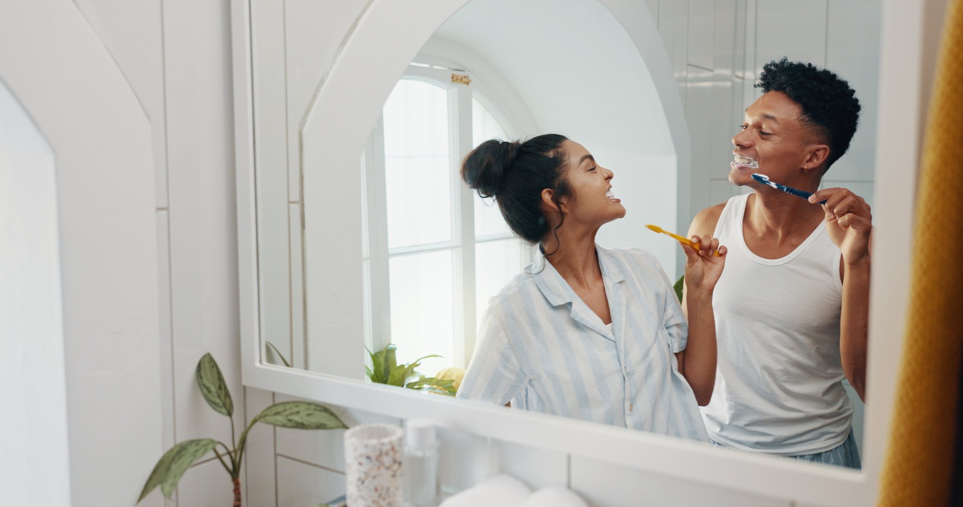 Brushing teeth, having fun and morning with couple in bathroom for dental hygiene or oral care. Happy, love and mirror with playful people in home together to prevent cavity or gum disease for health