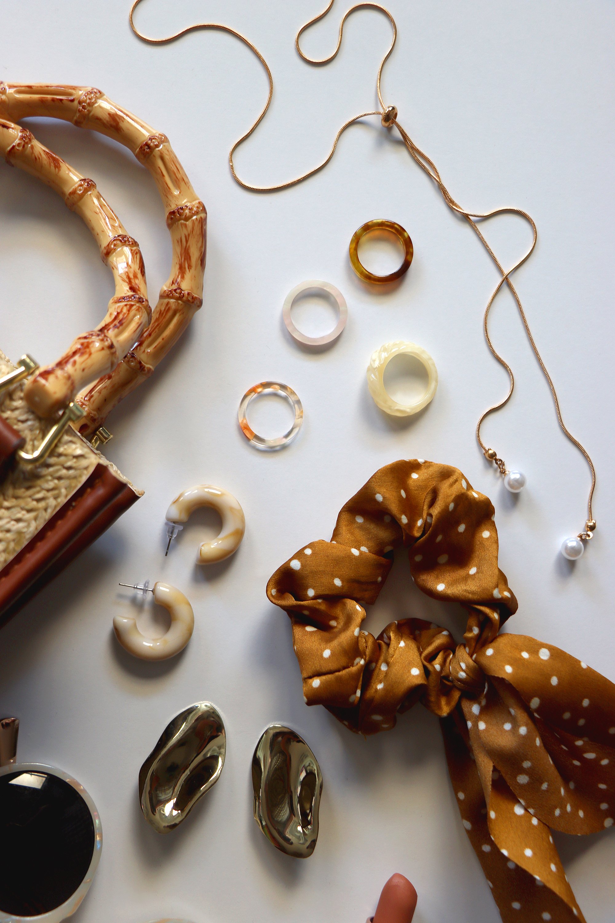 Wicker purse, sunglasses, scrunchie, lipstick and various gold and neutral jewelry on white background. Top view.