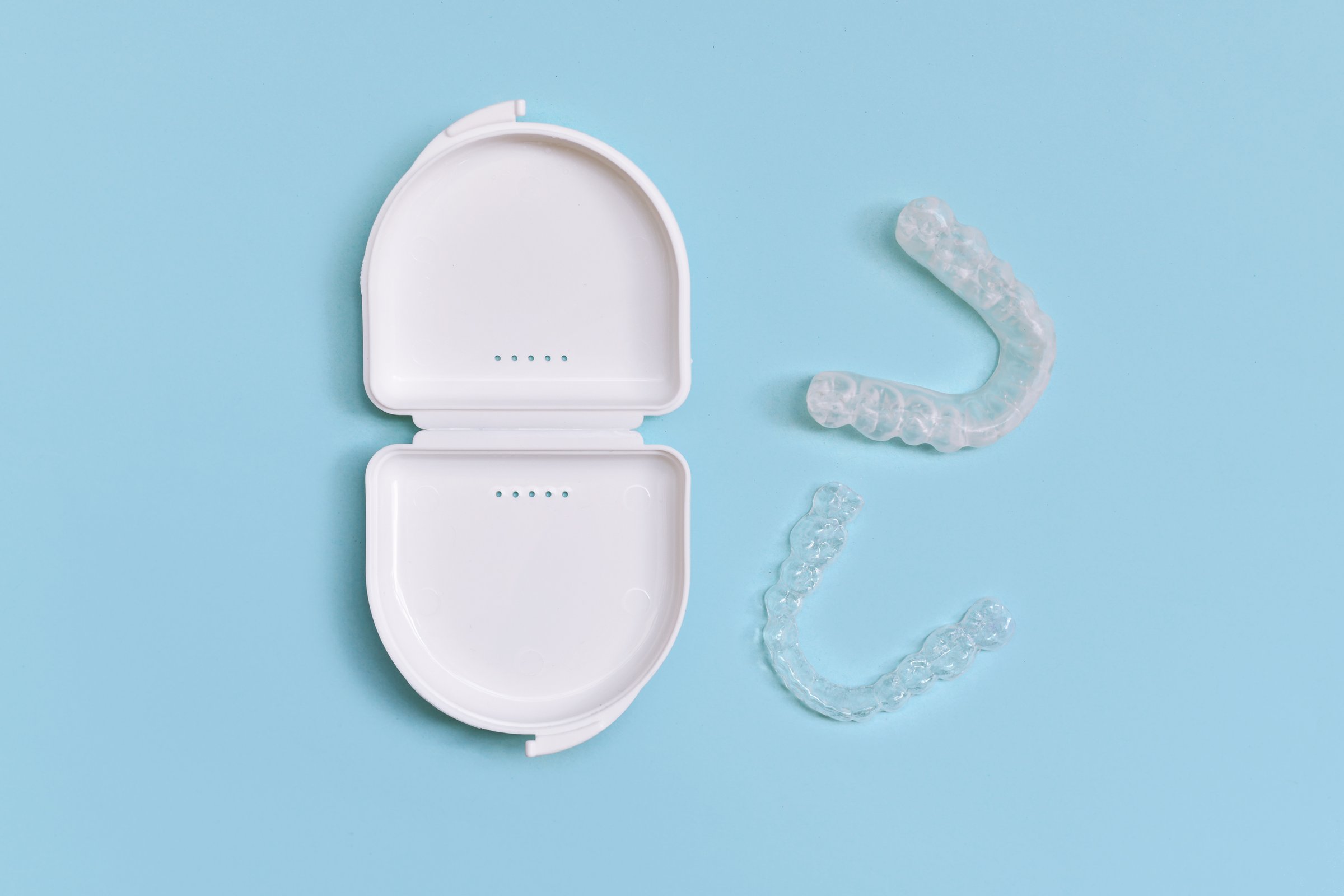 Customized transparent dental teeth bite guard clear aligners for lower jaw in white case on blue background
