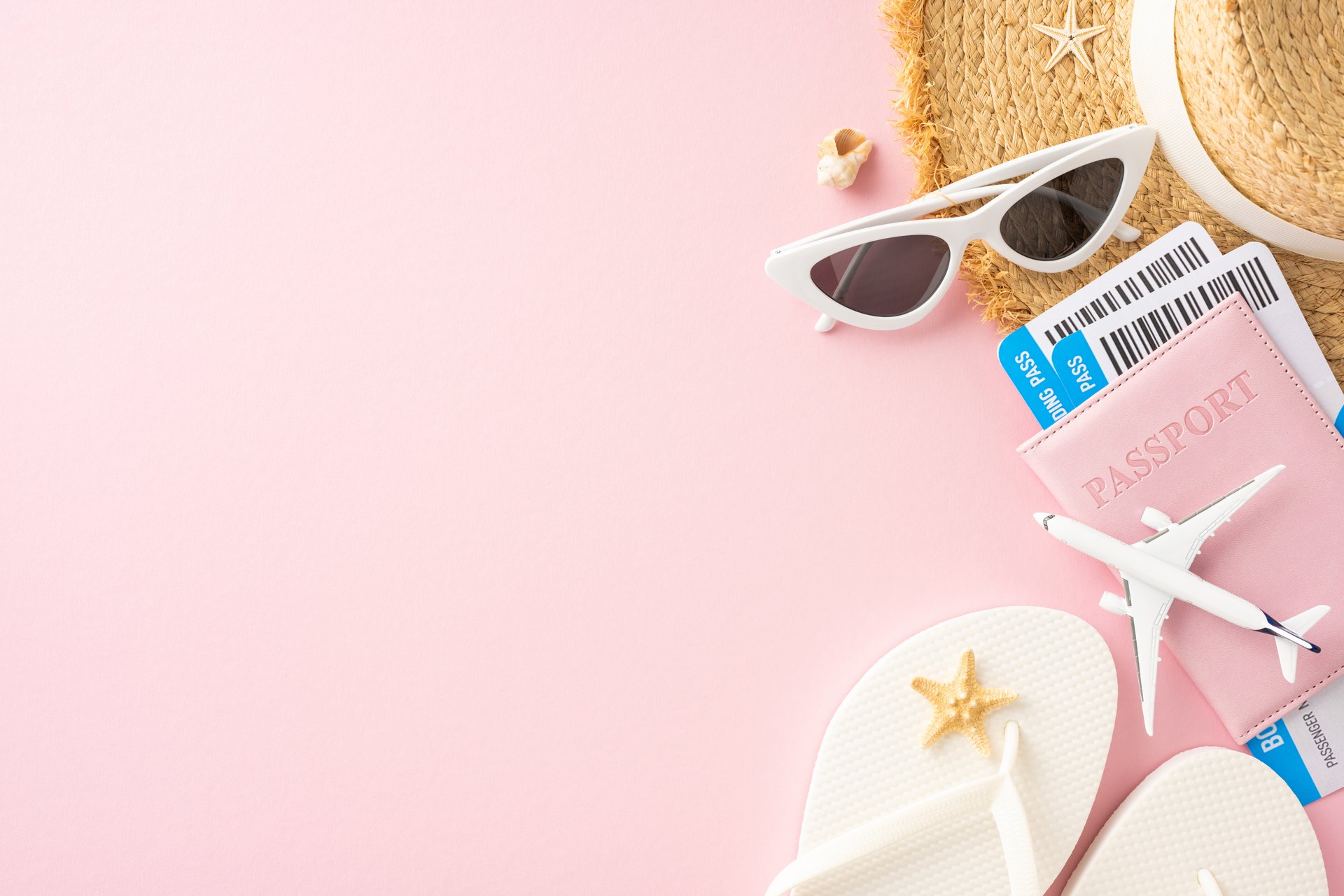 Summer vacation concept with travel essentials including a passport, sunglasses, flip-flops, and a toy airplane on a pink background