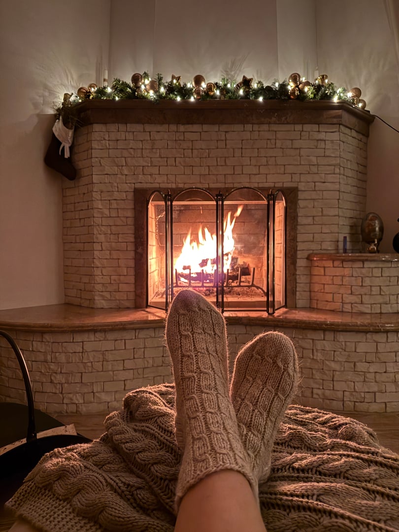 Cozy mood on Christmas Eve with fire in fireplace, Christmas tree. Women's feet in cozy wool socks warming up by fireplace