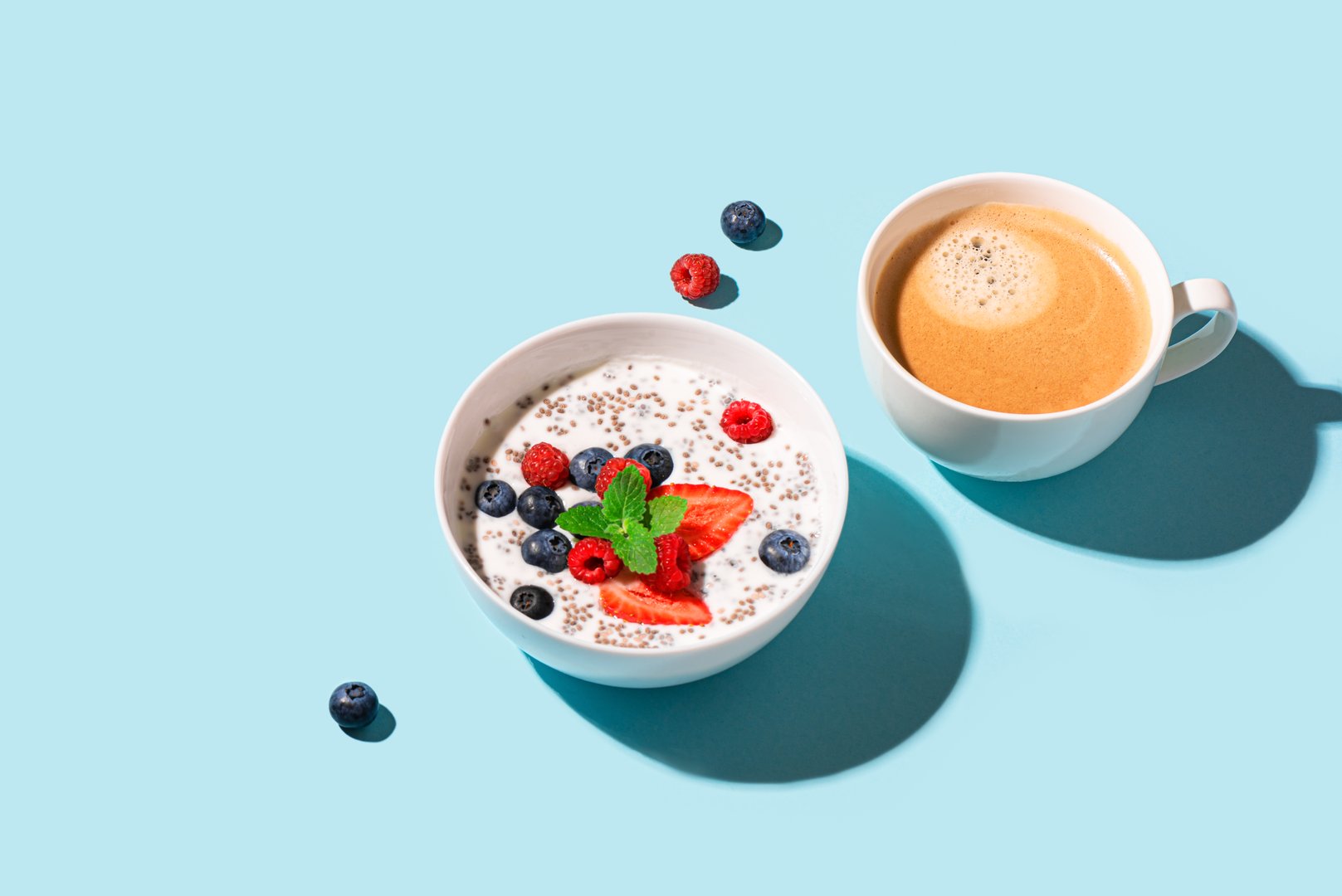 Healthy breakfast with chia bowl and cappuccino coffee on blue background, trendy design with hard light. Chia pudding with berries. Healthy plant based diet, fitness summer recipe.