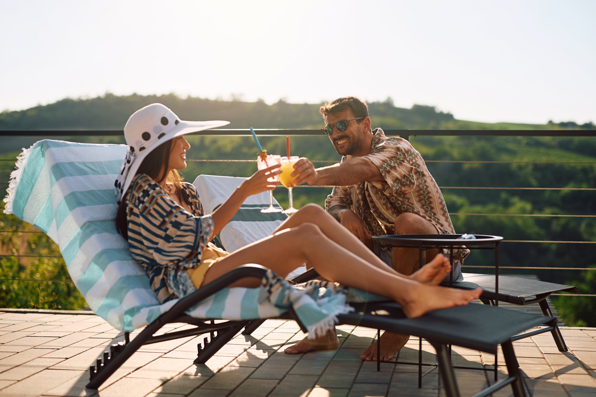 Happy man and his girlfriend toasting with summer cocktails while relaxing on a terrace.