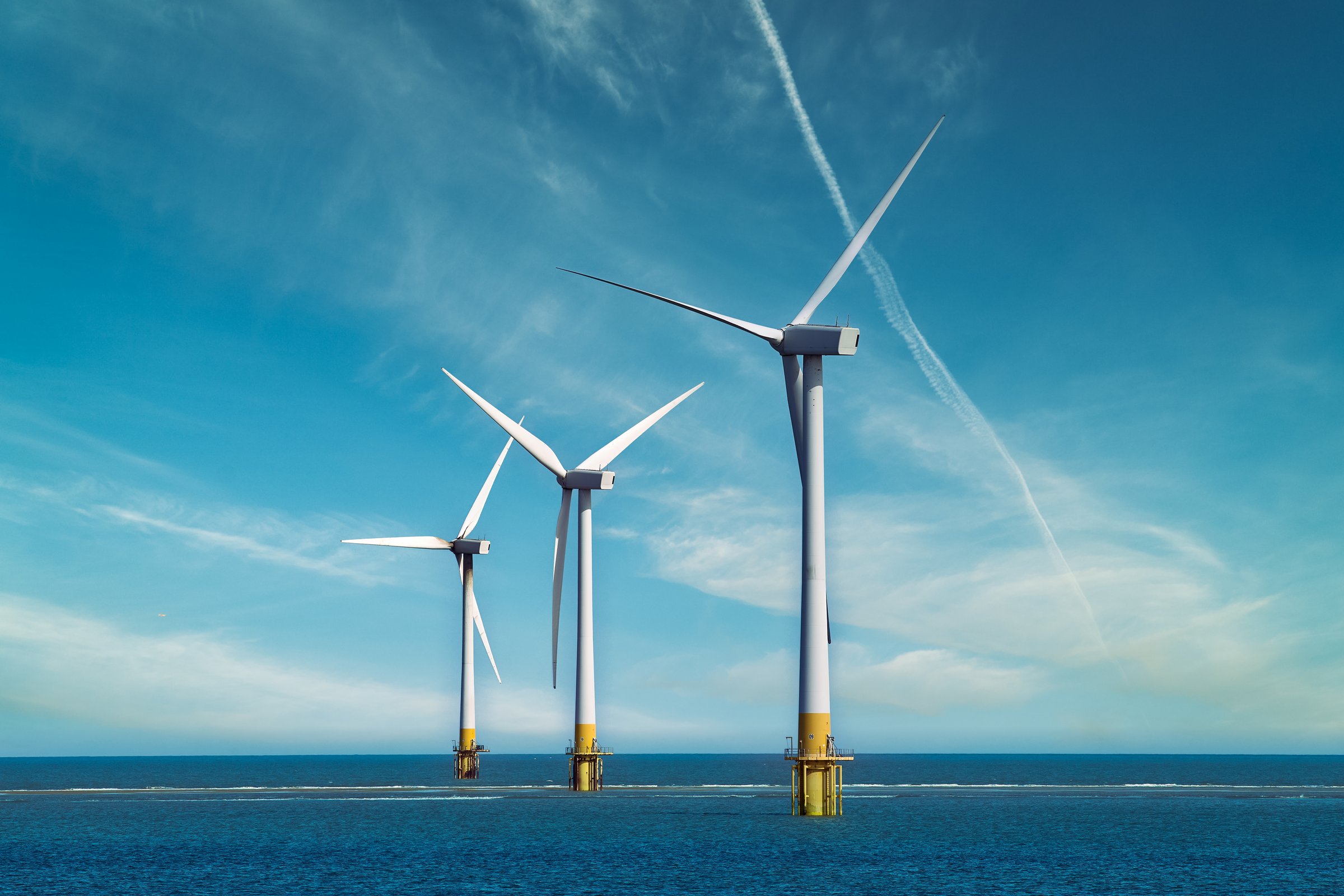 Three offshore wind turbines standing in the sea, with clear blue sky. Wind Turbines at Sea. Sustainable energy production.