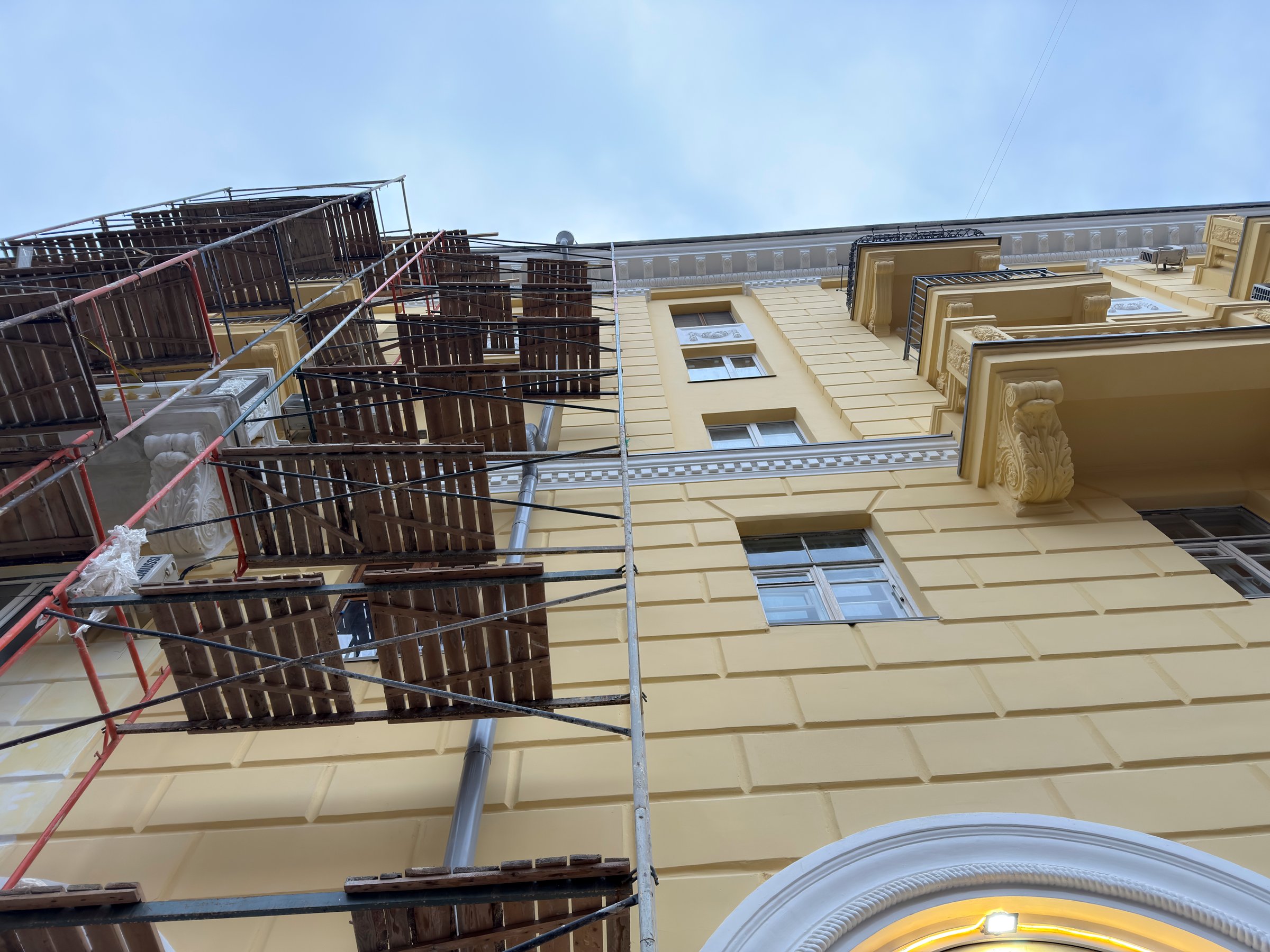Scaffolding surrounds a yellow building while workers perform repairs from above.