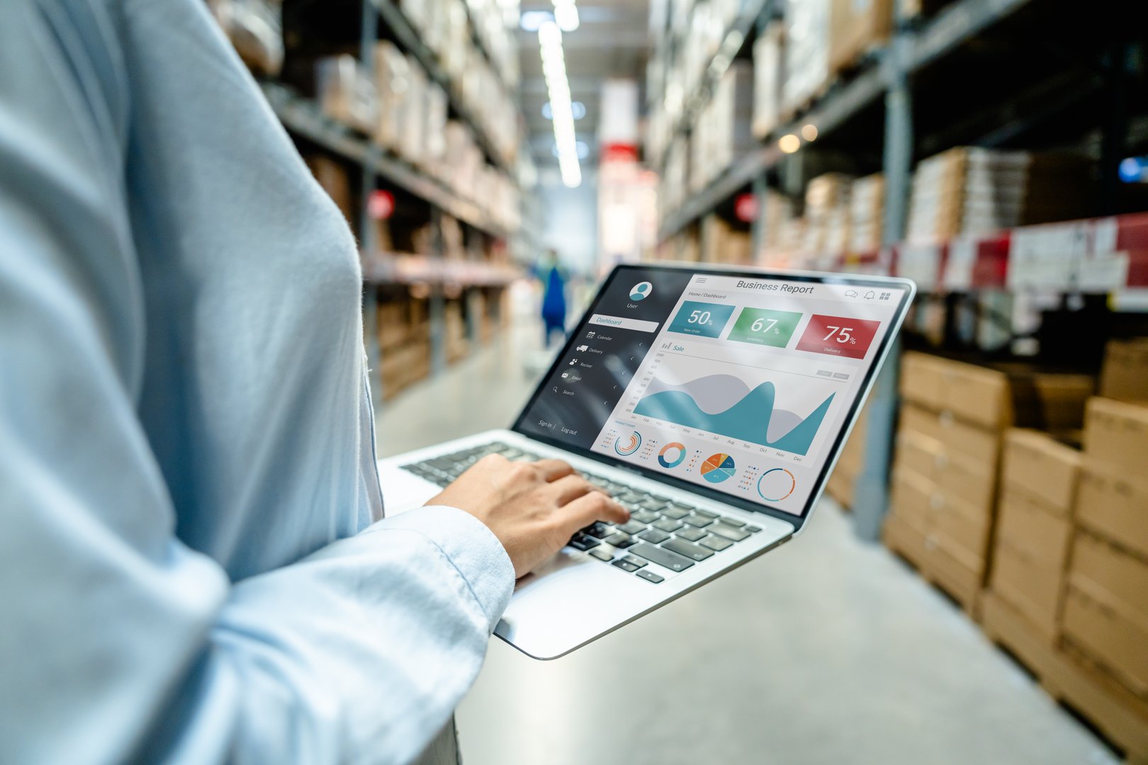 Employee using a laptop with business analytics dashboard in a modern warehouse