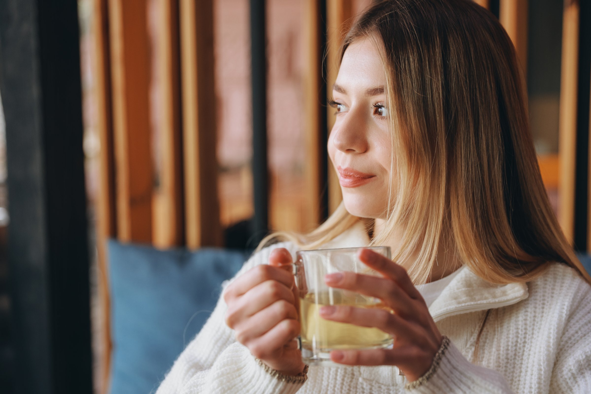 Serene young woman savoring a warm cup of herbal tea, finding comfort and tranquility in a cozy cafe atmosphere