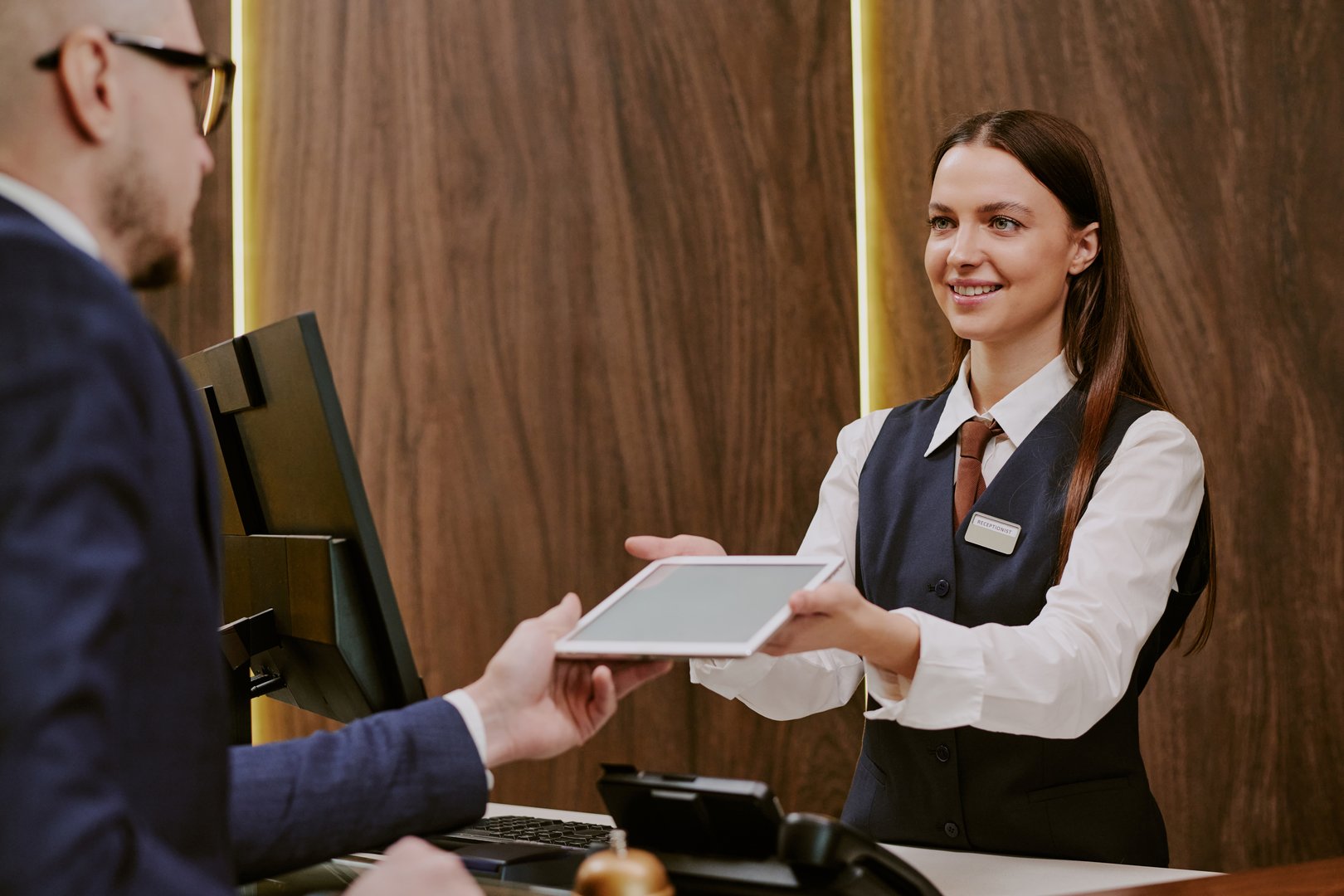 Medium close up of unrecognizable male hotel guest taking tablet from female receptionist hands