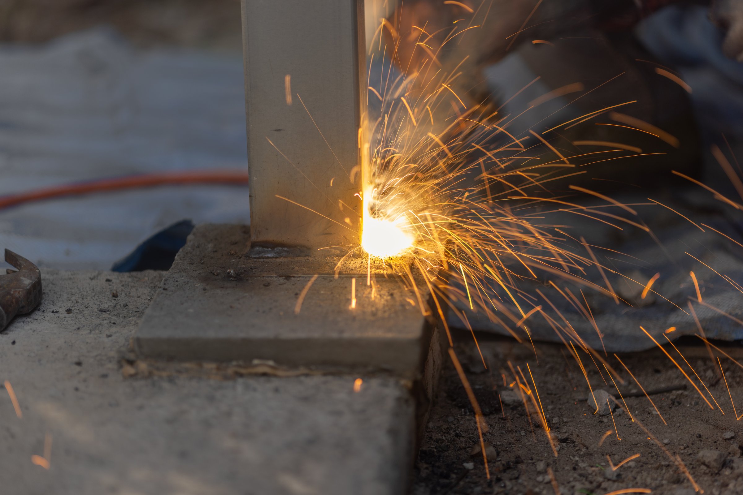 Worker welding steel post in construction site.