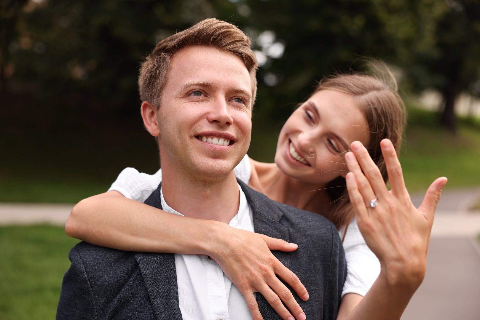 Marriage proposal. Smiling woman showing engagement ring and hugging her fiance outdoors