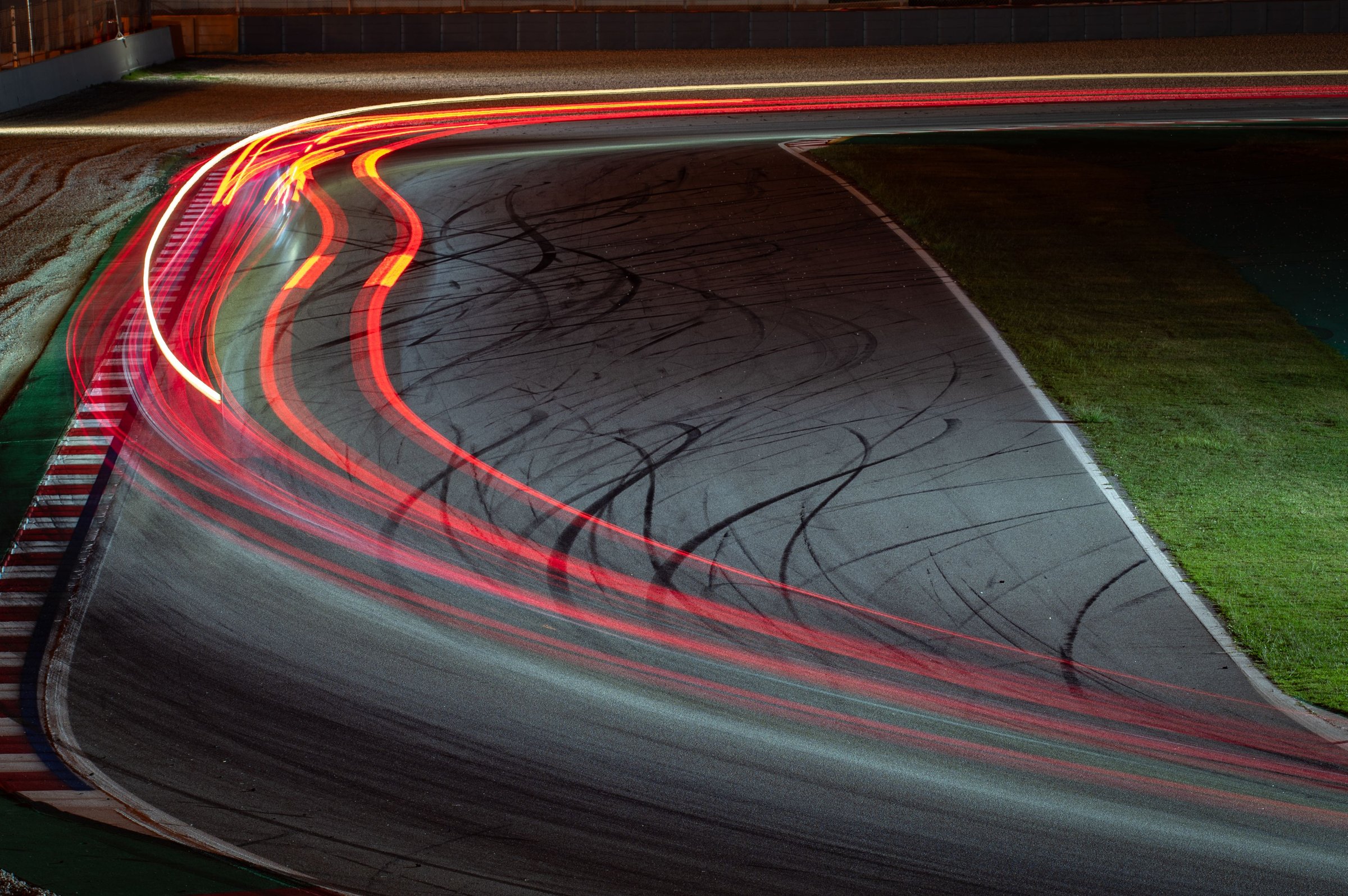 Long exposure night photography that shows the traces of light left by the racing cars as they pass through the curve.